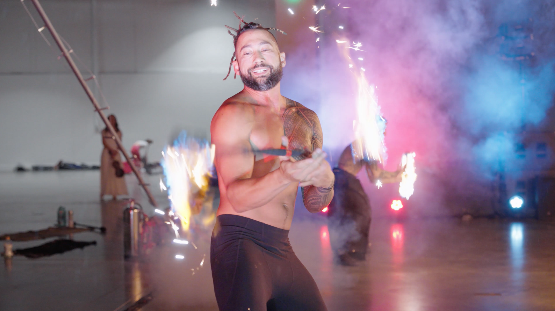 A shirtless man is standing in front of a bunch of fireworks.