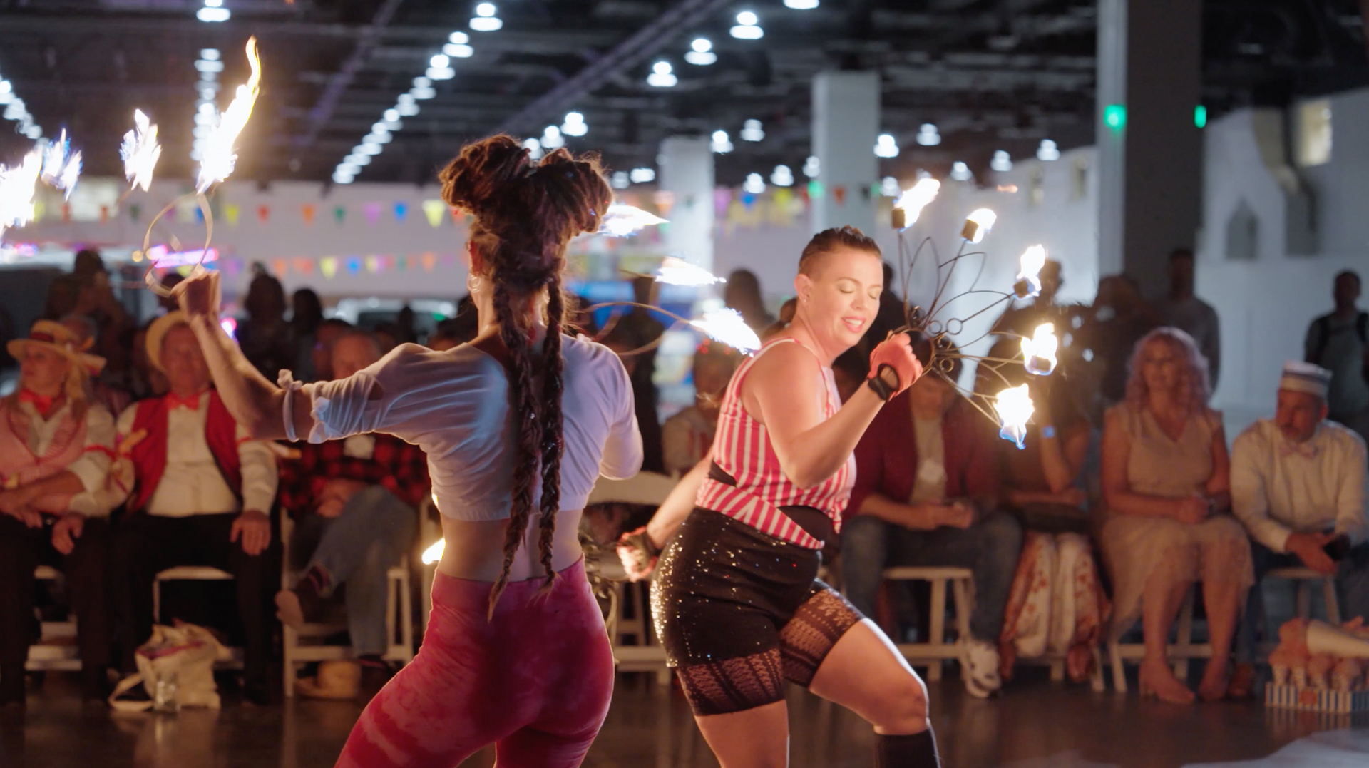 Two women are dancing with fire sticks in front of a crowd.