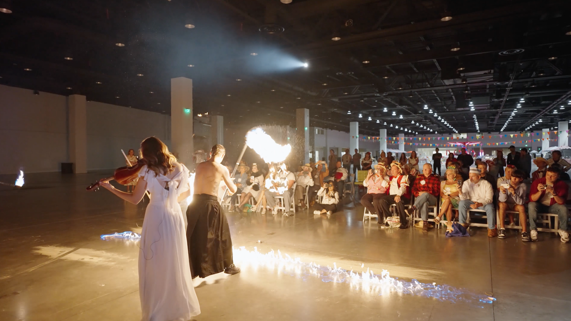 A man and a woman are playing violins in front of a crowd of people.