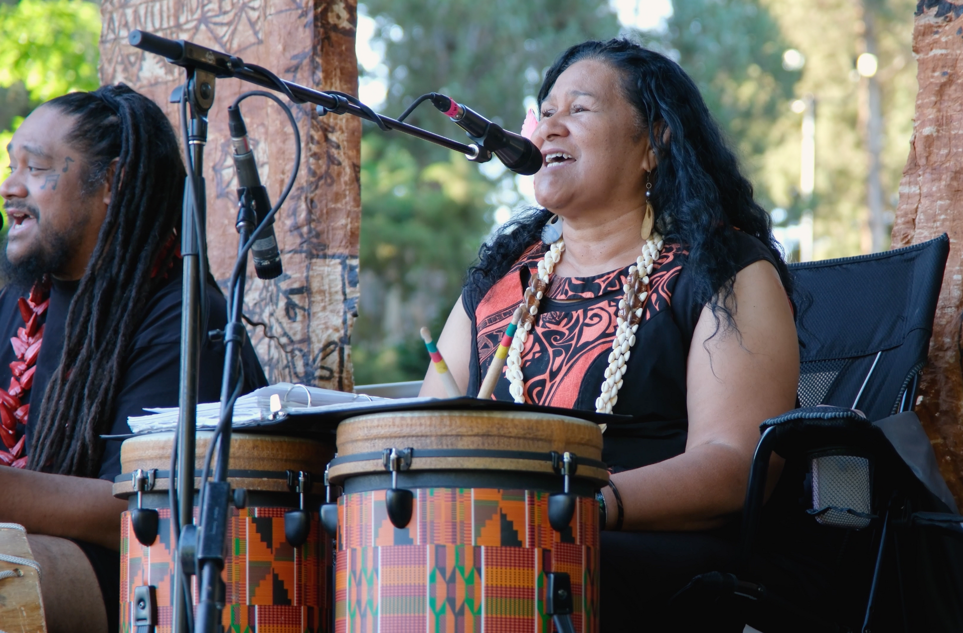 A man and a woman are playing drums and singing into microphones.