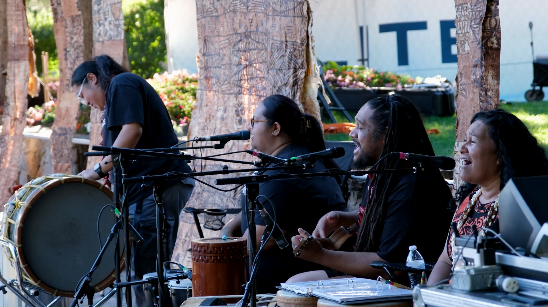A group of people are playing drums and singing into microphones.