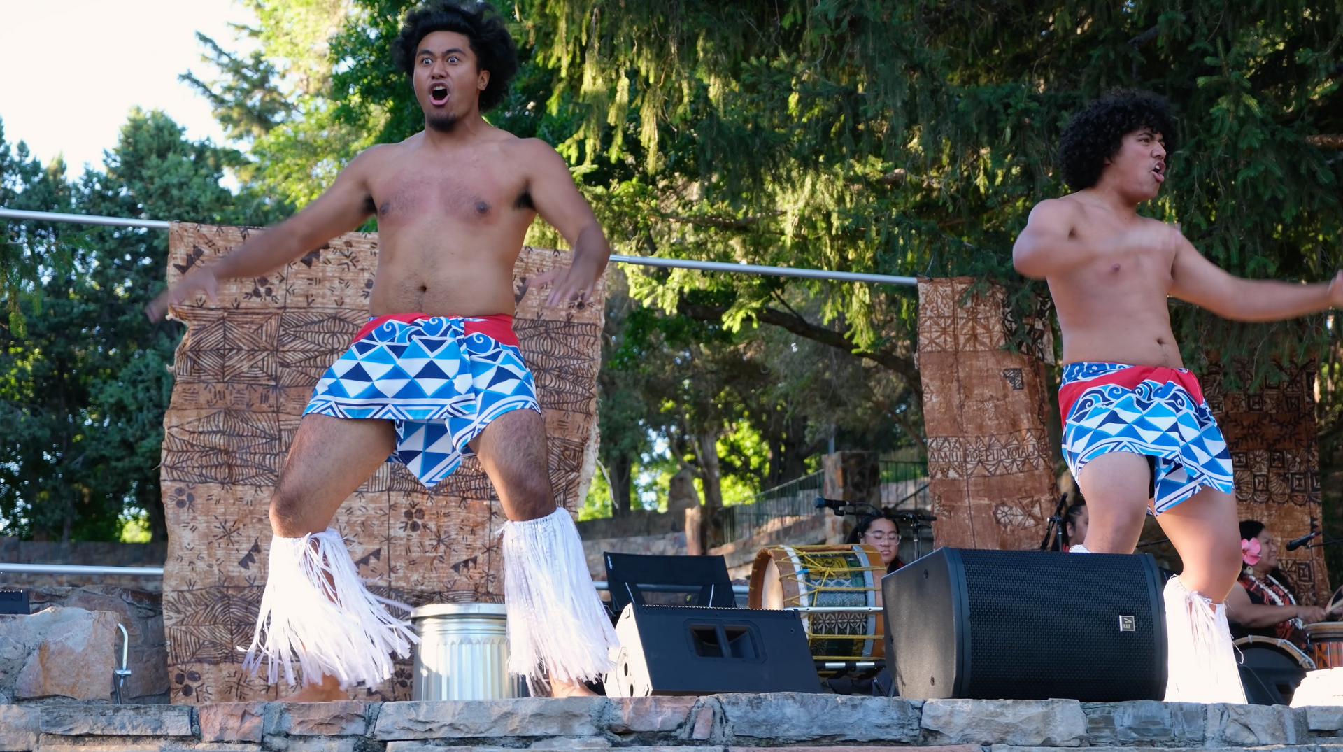 Two shirtless men are dancing on a stage in front of a speaker