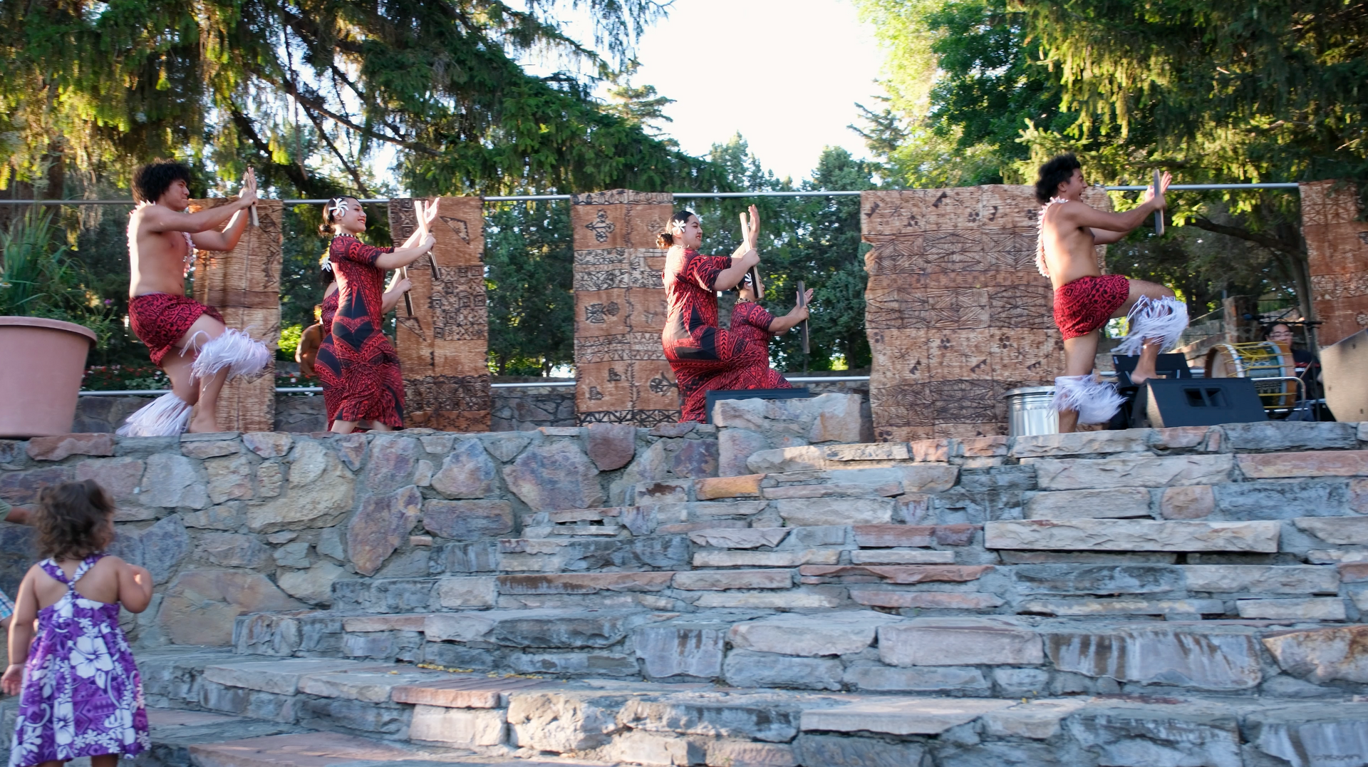 A little girl watches a group of people perform on stone steps