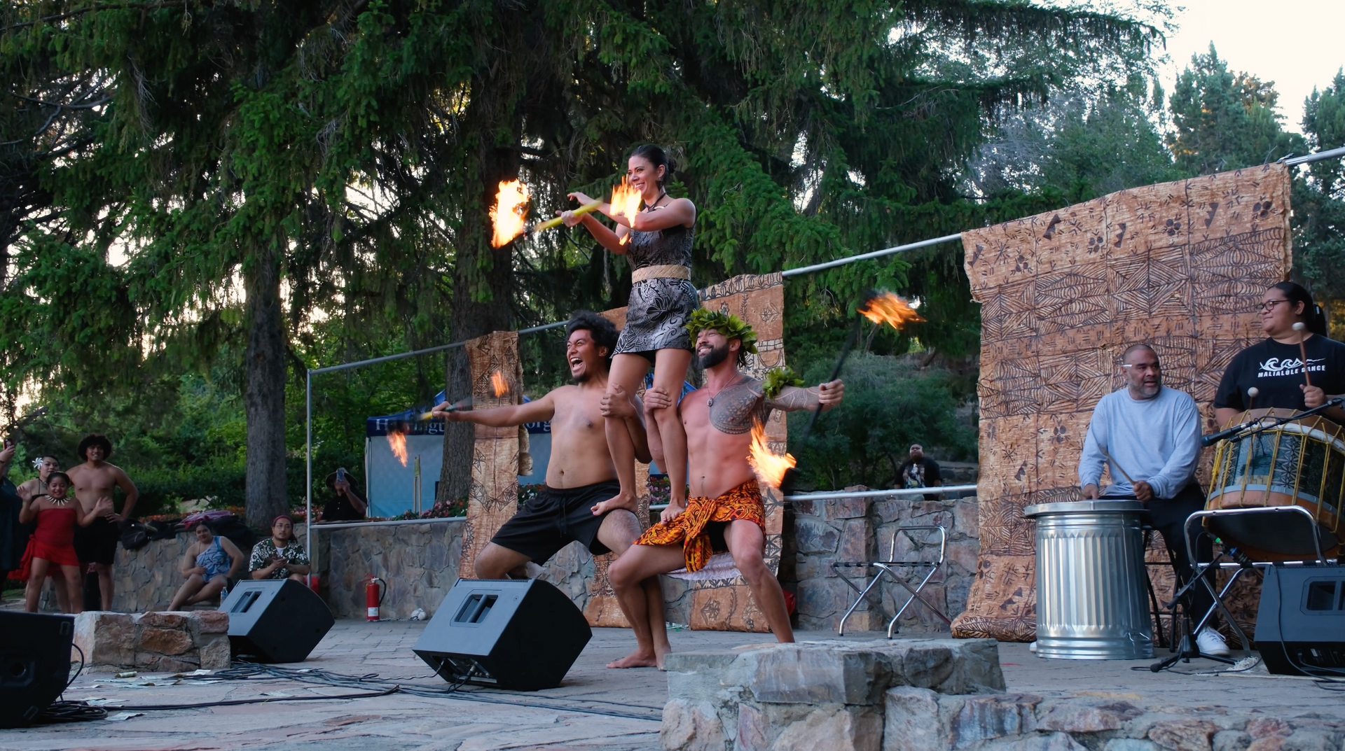 Three fire performers are stacked on top of each other spinning fire.