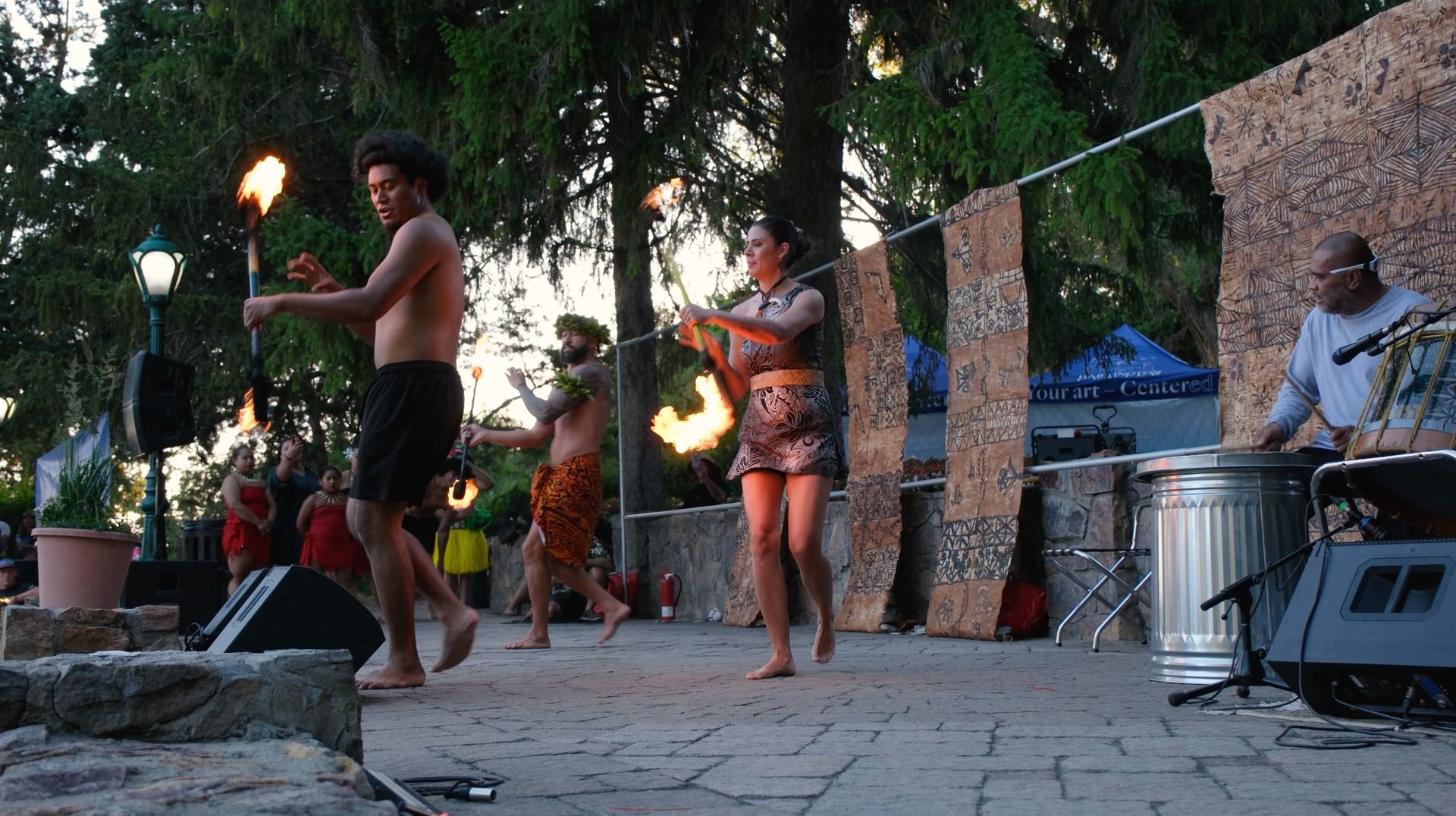 A group of people are dancing on a stage with fire torches.