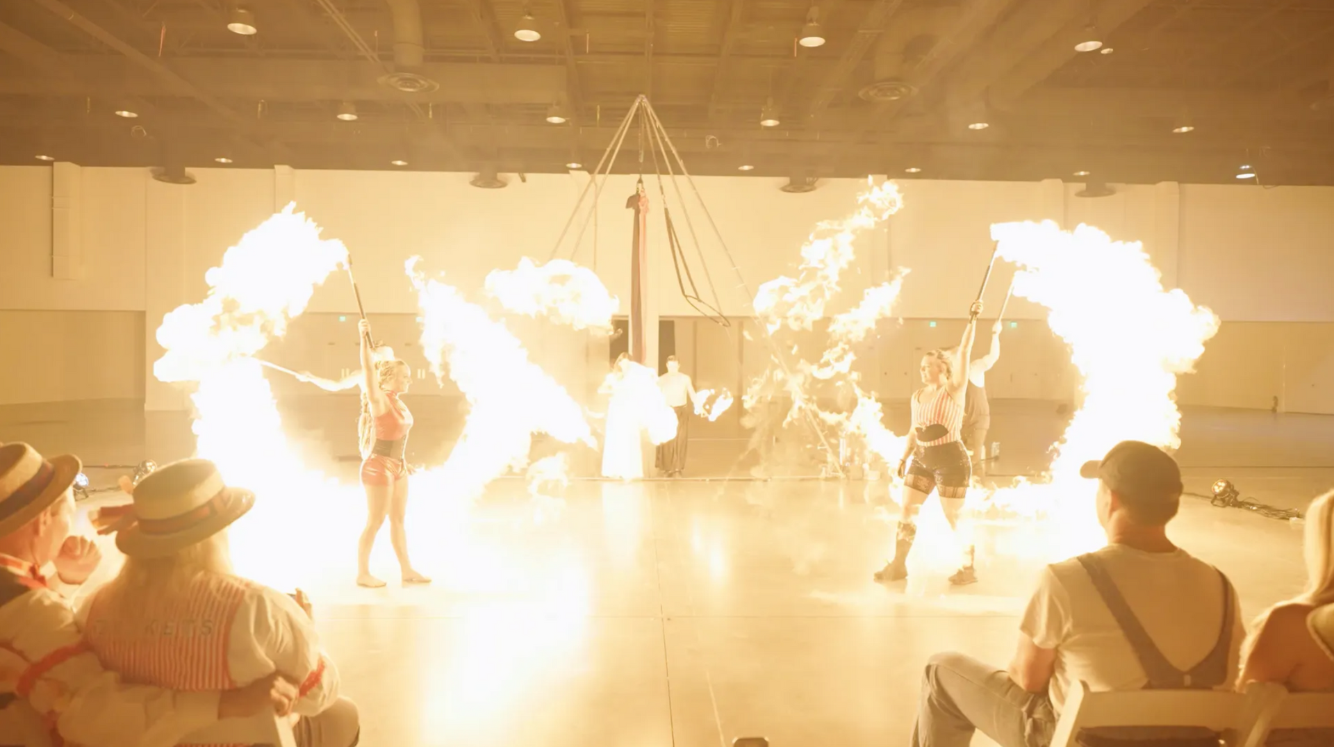 A group of people are watching a fire show in a large room.