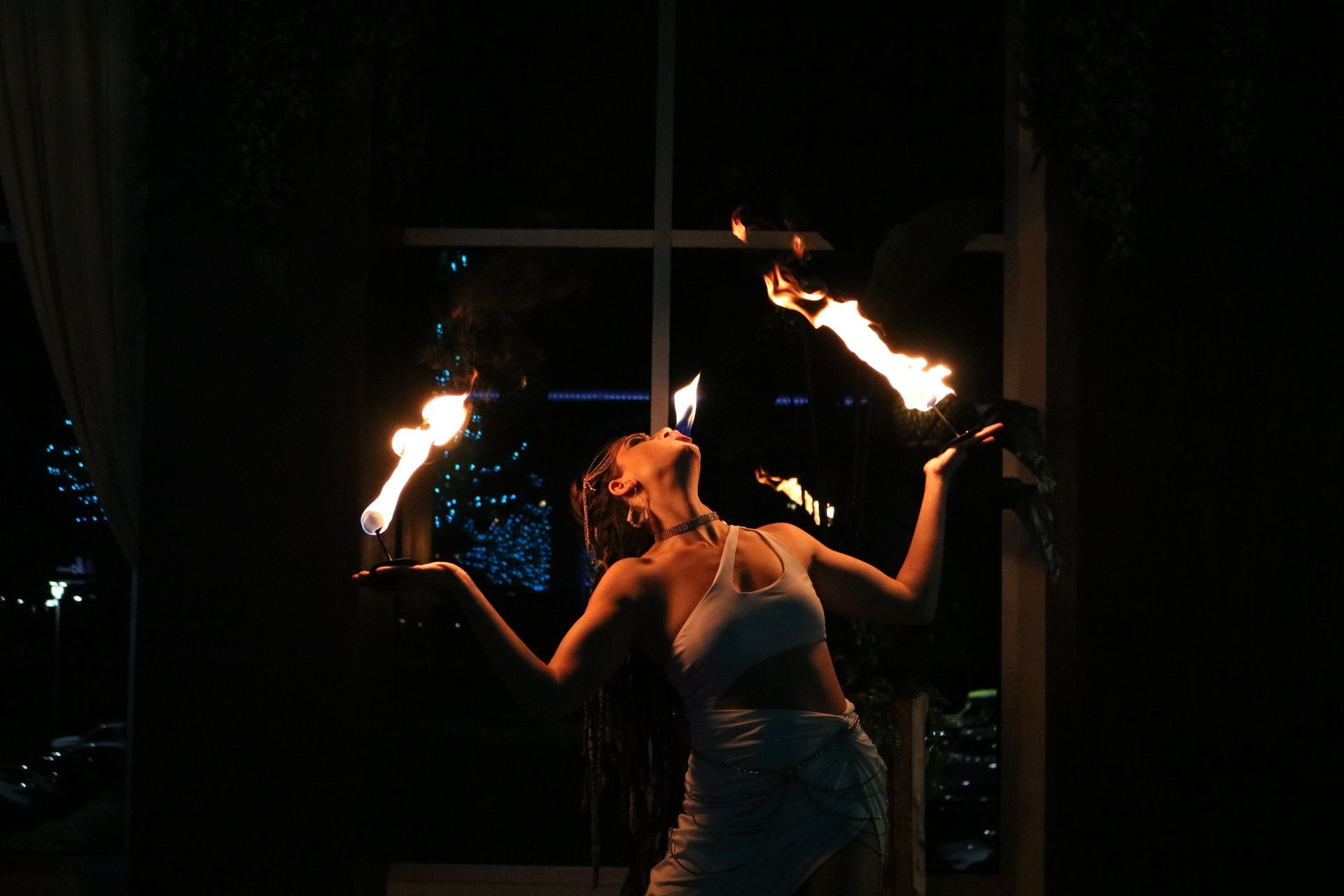 A woman is holding two fire torches in her hands in a dark room.