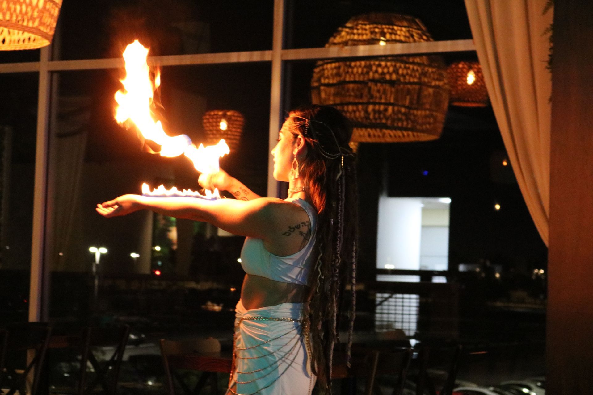 A woman is holding a fireball in her hand in front of a window.