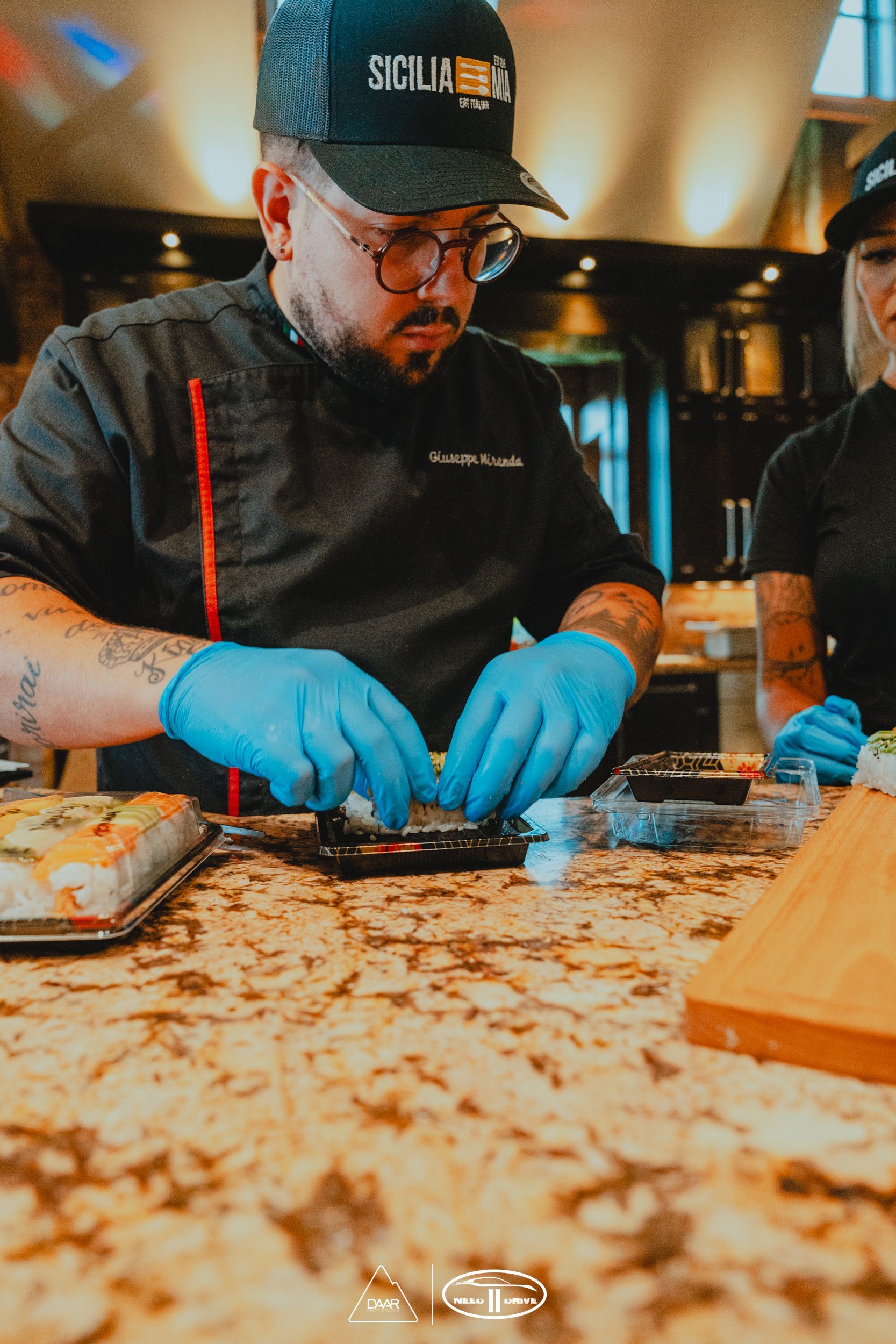 A man wearing a hat and blue gloves is preparing food on a counter.