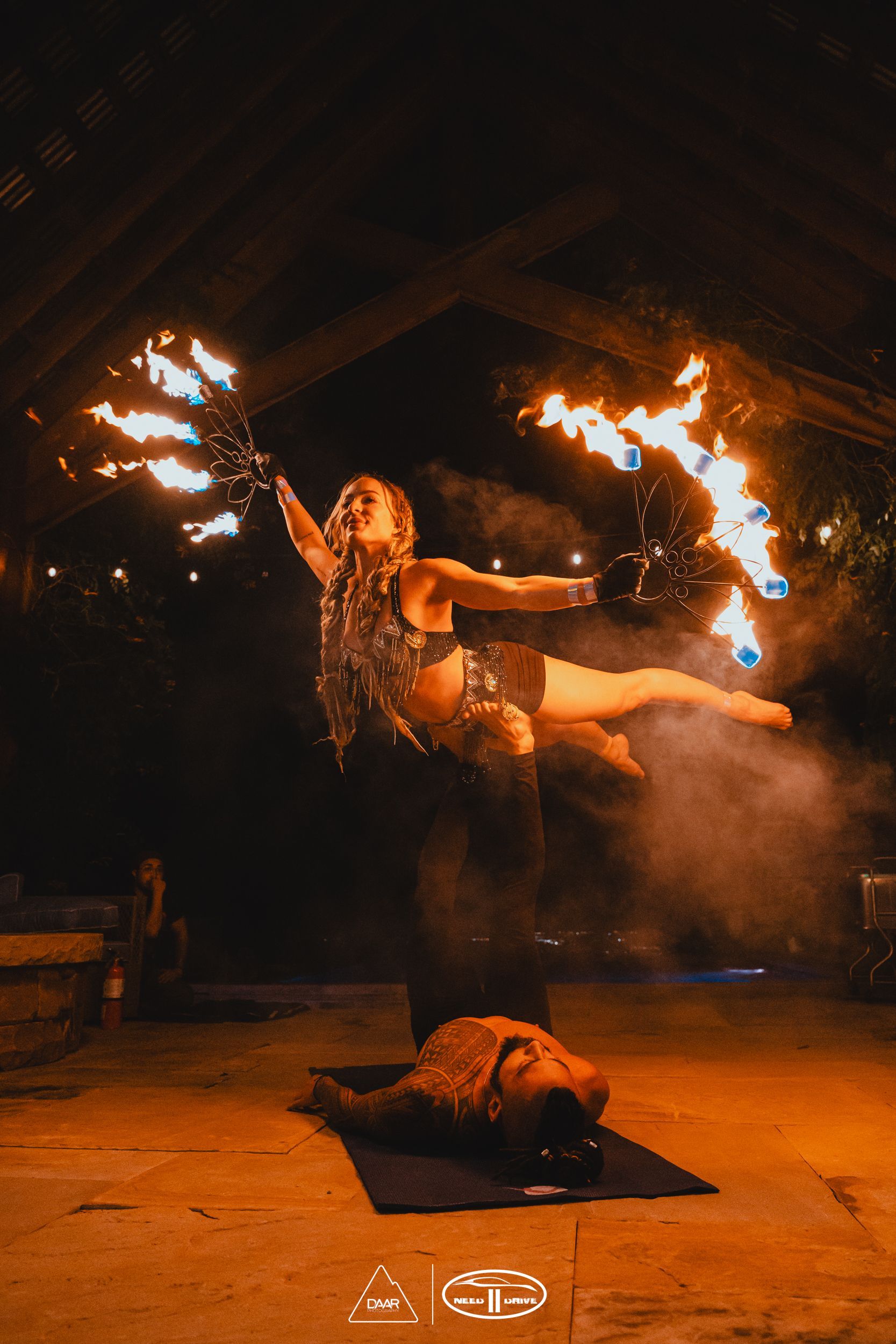 A woman is standing on a man 's shoulders while holding a fireball.