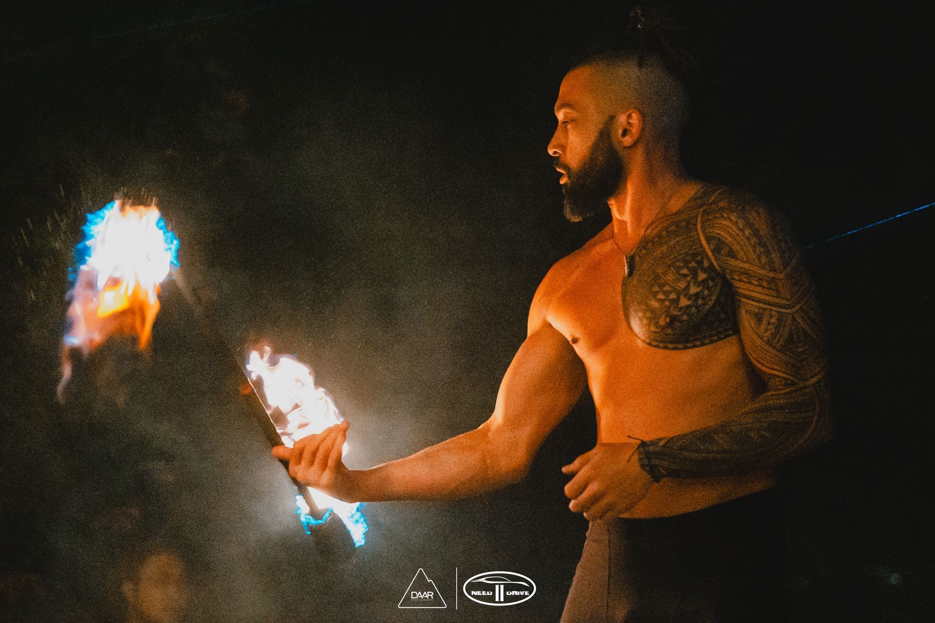 A shirtless man is holding a torch in the dark.