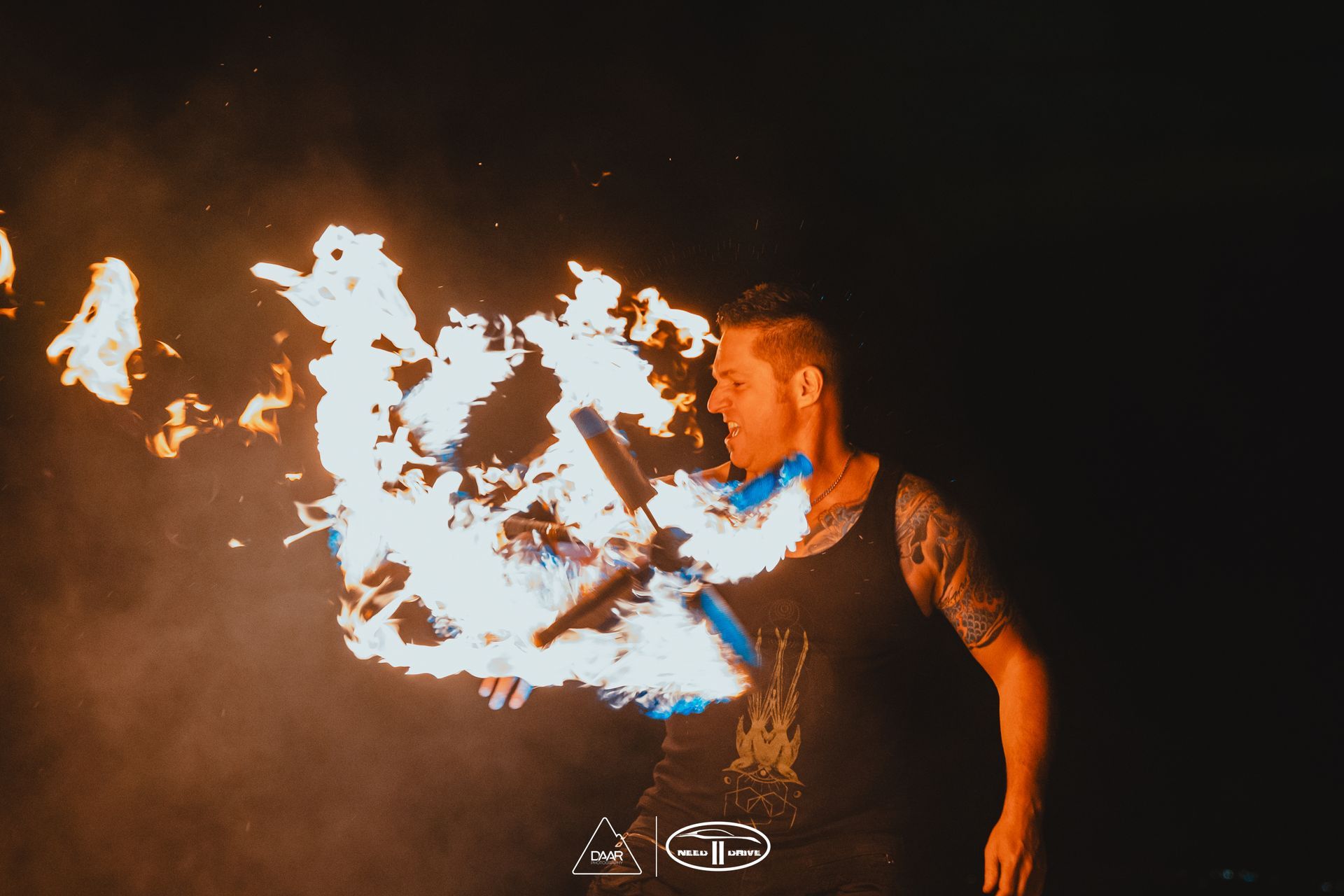 A man with a tattoo on his arm is holding a torch in his mouth.