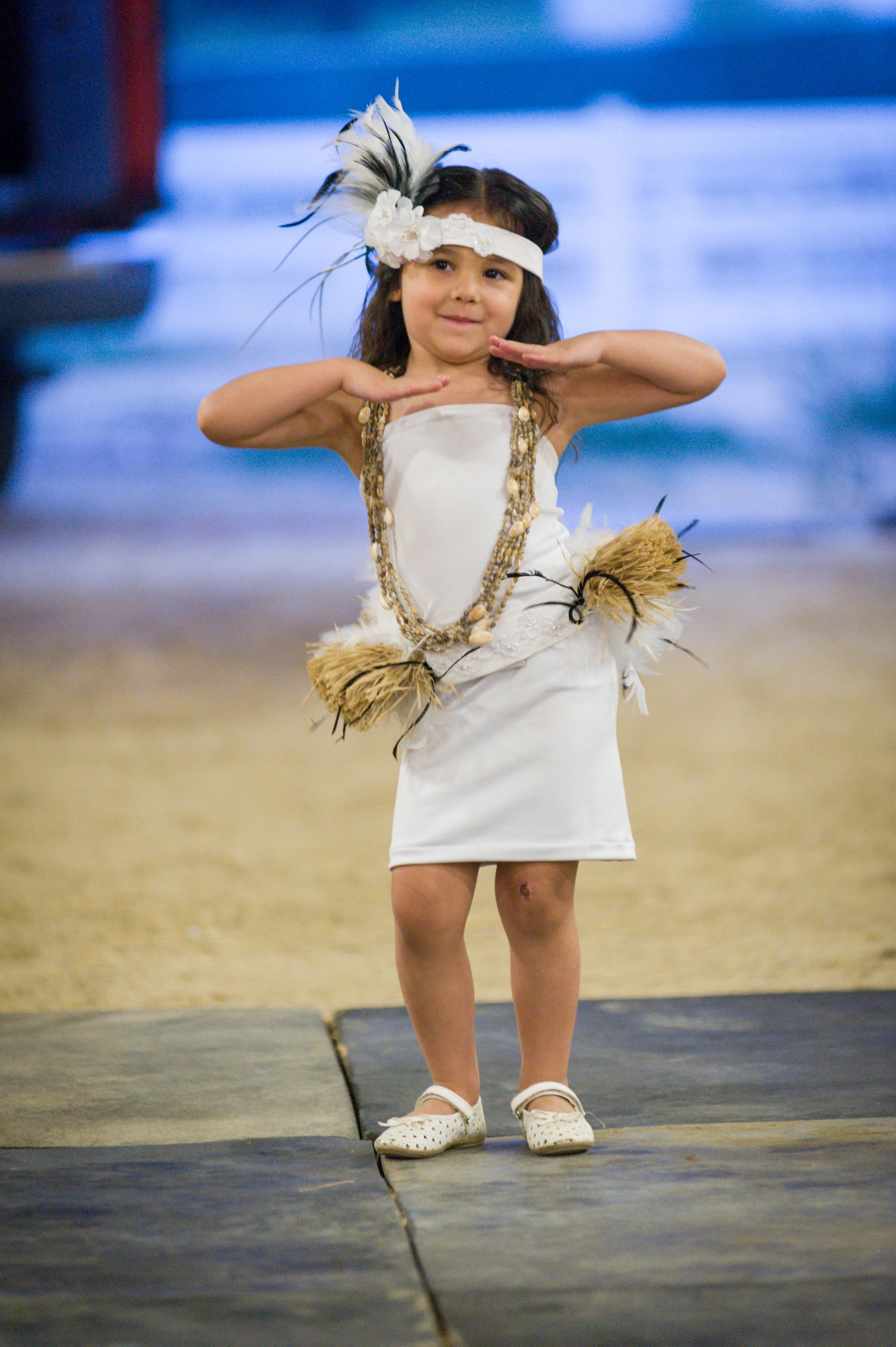 A little girl in a white dress is walking down a runway.