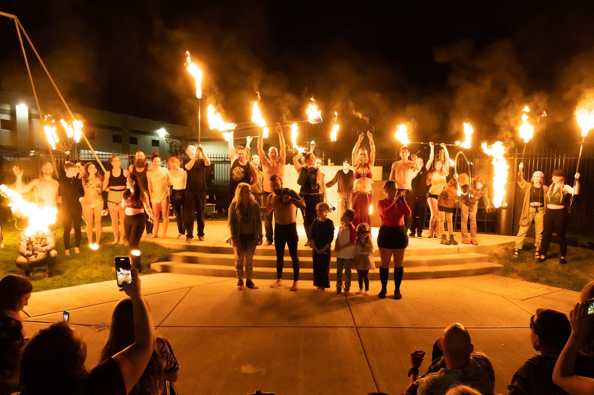 A group of people are standing in front of a fire at night.