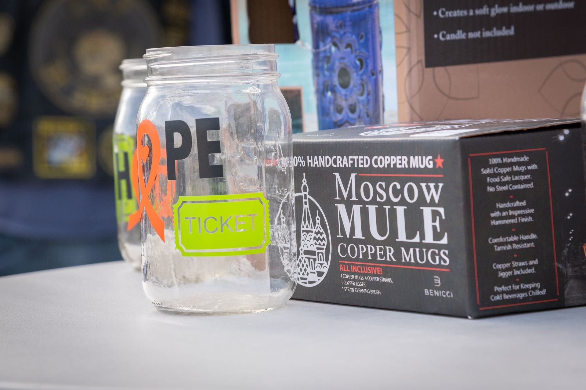 Three mason jars are sitting on a table next to a box of moscow mule copper mugs.