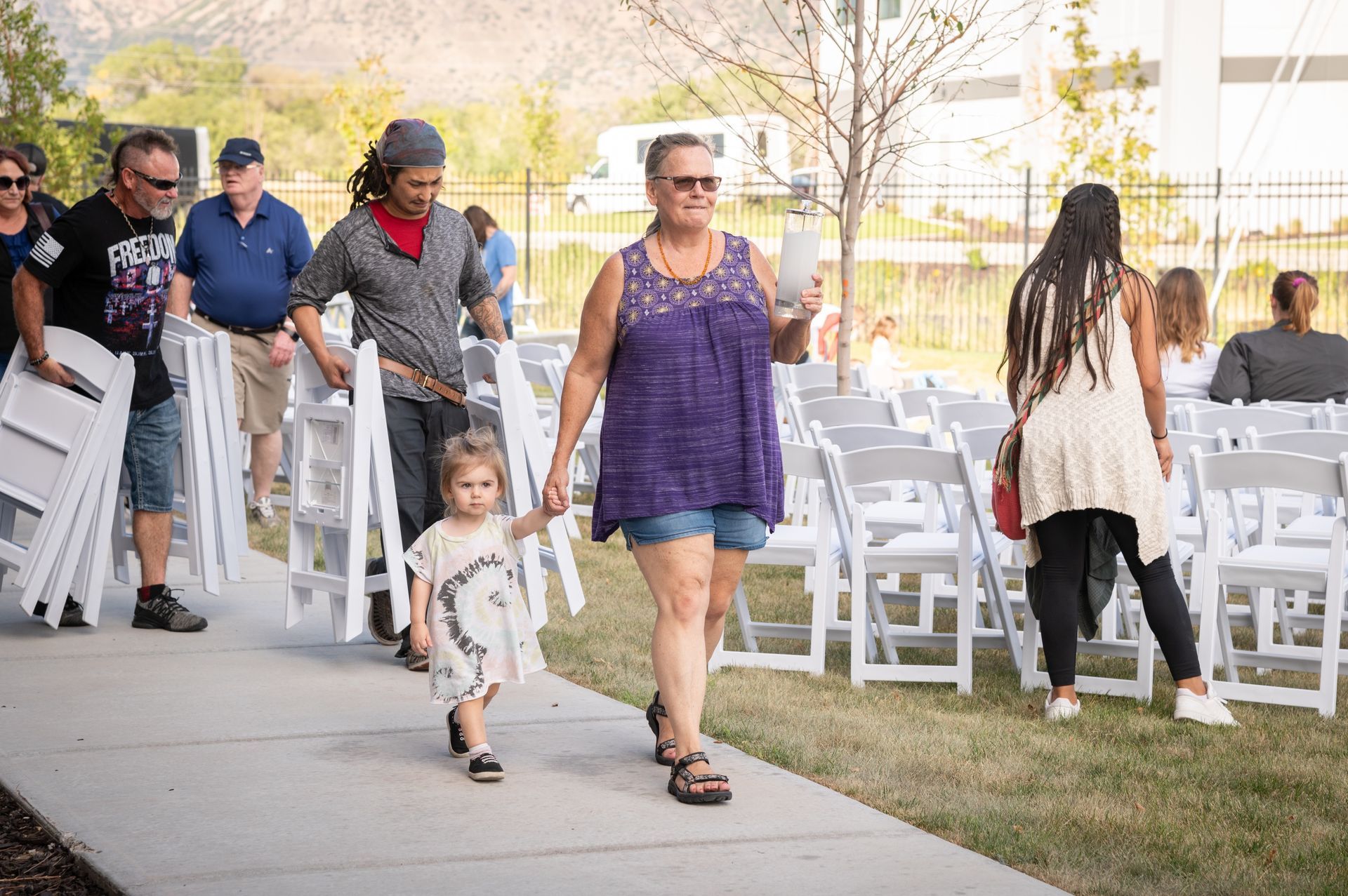 A group of people are walking down a sidewalk carrying folding chairs.