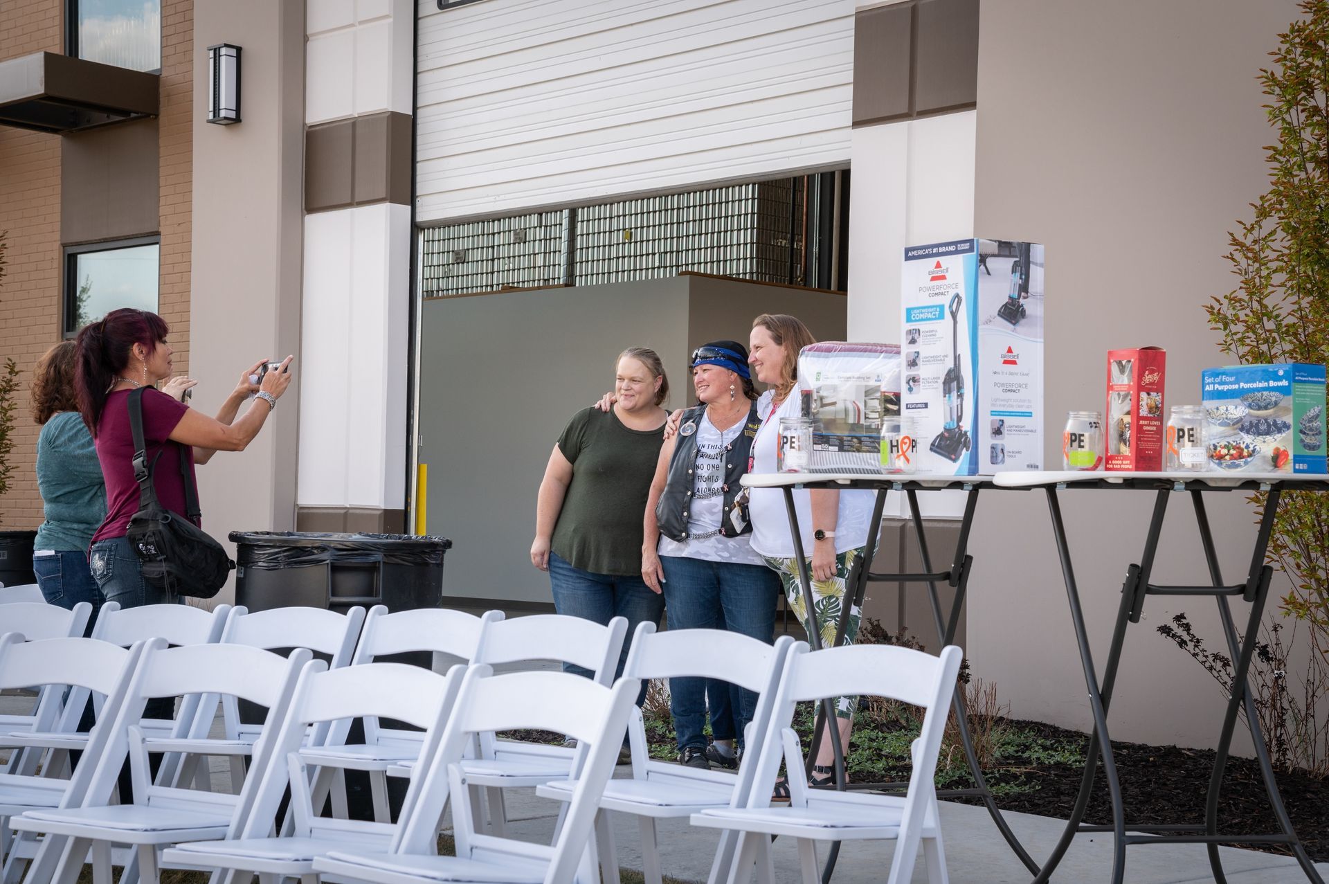 A group of women are standing in front of a row of white chairs.