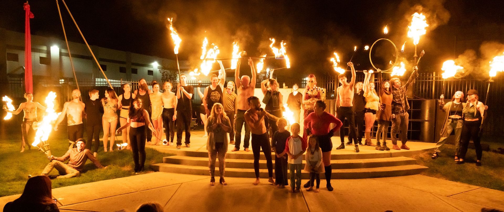 A group of people are standing in front of a fire at night.