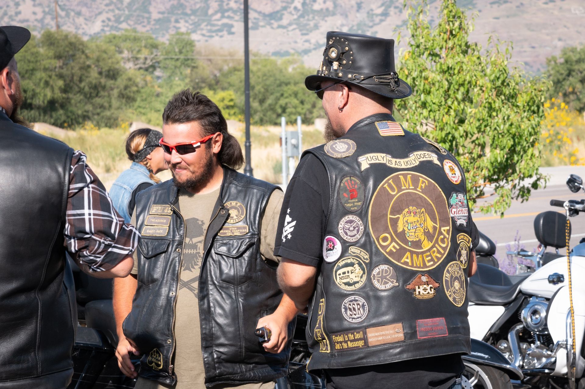 A man wearing a top hat and sunglasses is standing next to a motorcycle.