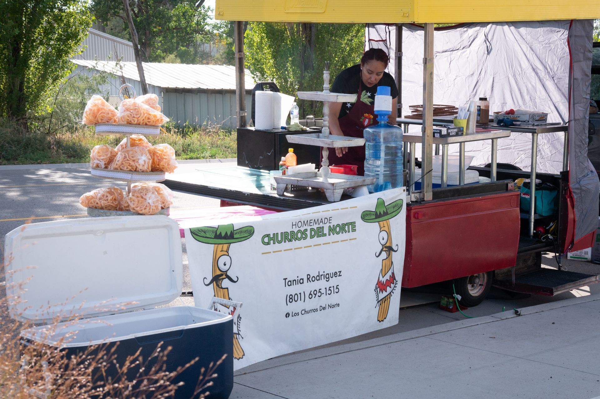 A man stands behind a food stand that says churros del norte