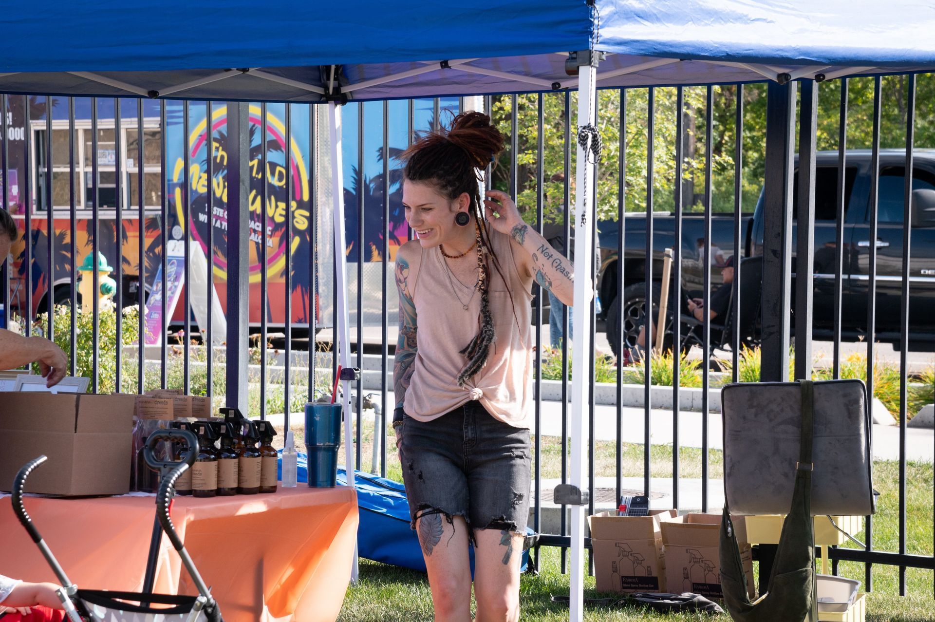 A woman is standing under a blue tent talking on a cell phone.