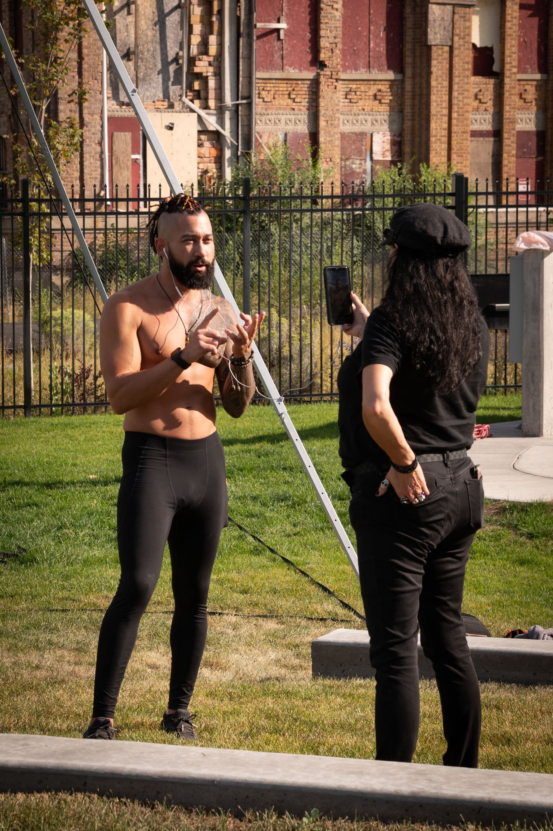 A shirtless man is talking to a woman in a park.