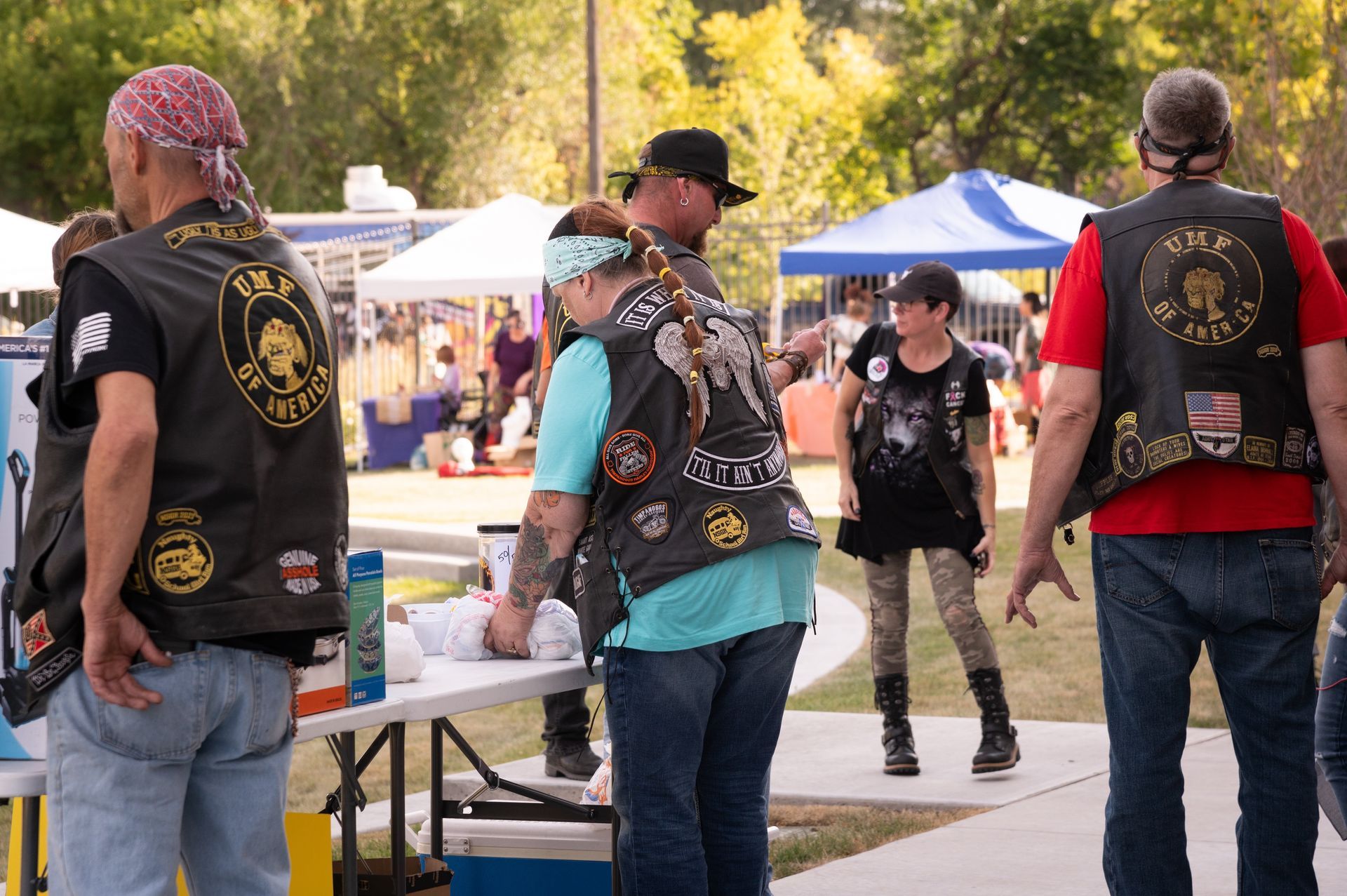 A group of people wearing vests with patches on them are standing in a park.