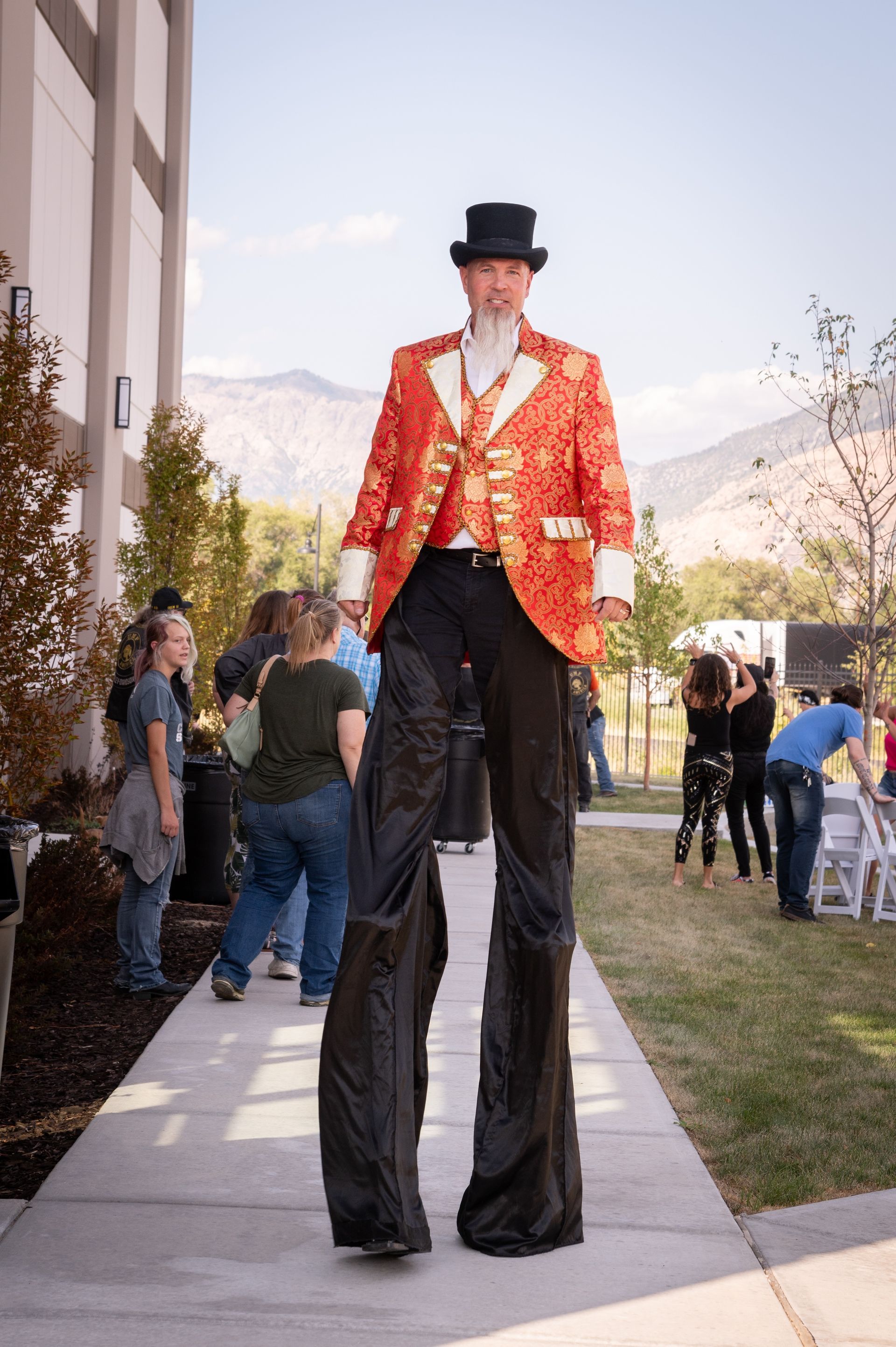 A man wearing a top hat and stilts is walking down a sidewalk.
