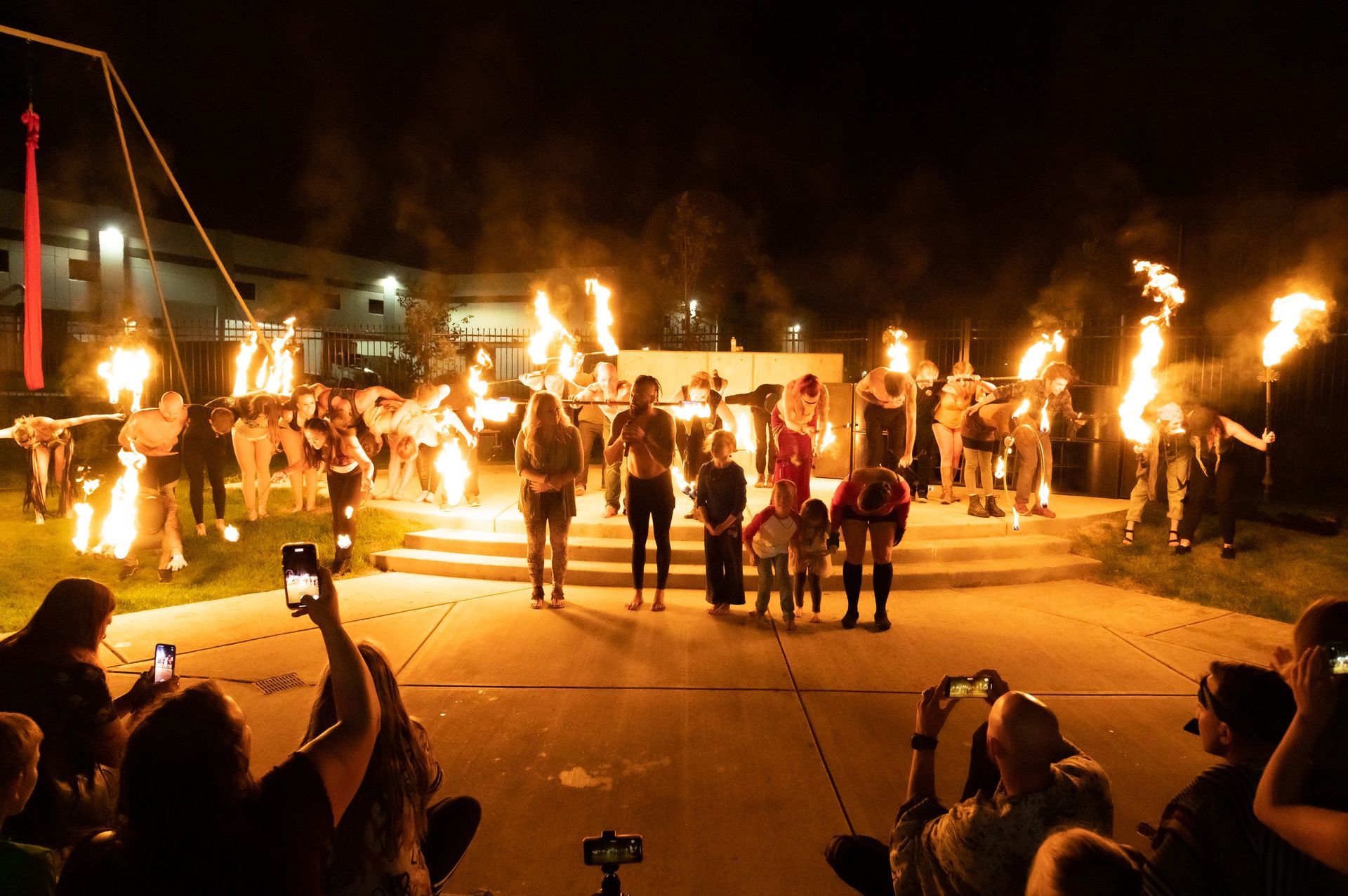 A group of people are standing in front of a fire show at night.