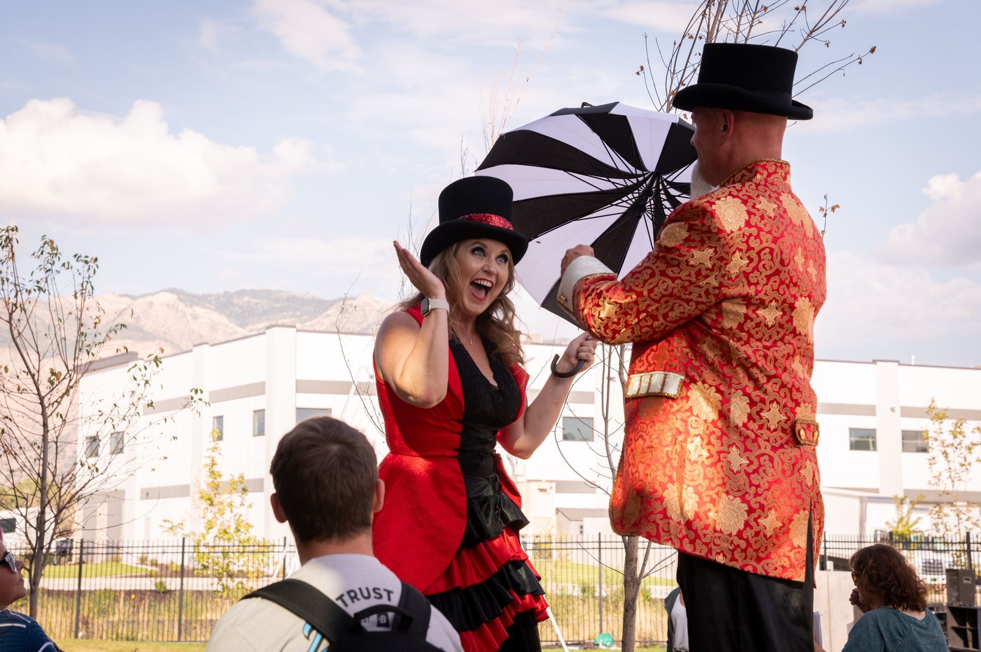 A woman in a red dress is standing next to a man on stilts holding an umbrella.