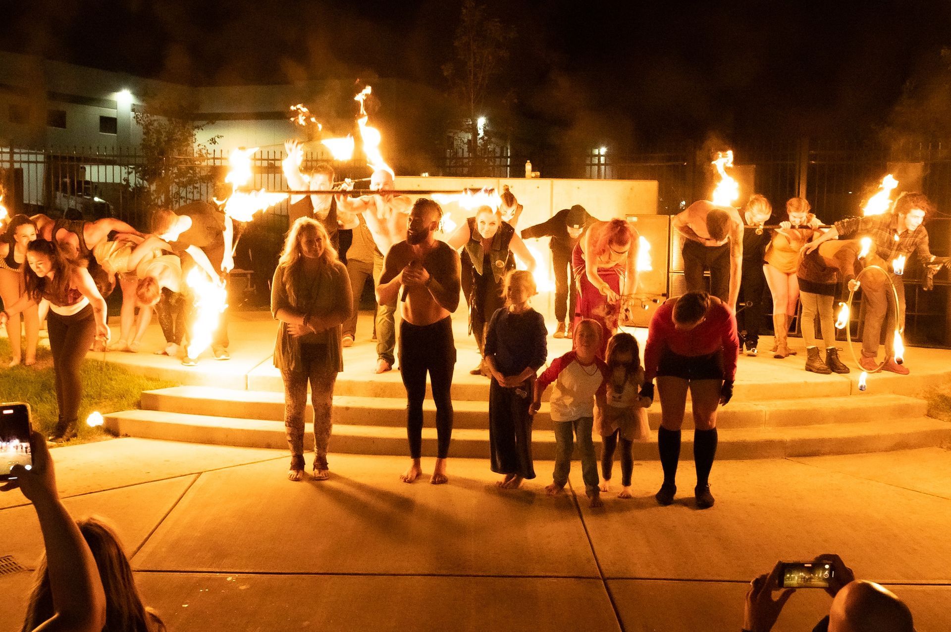 A group of people are standing in front of a fire at night.