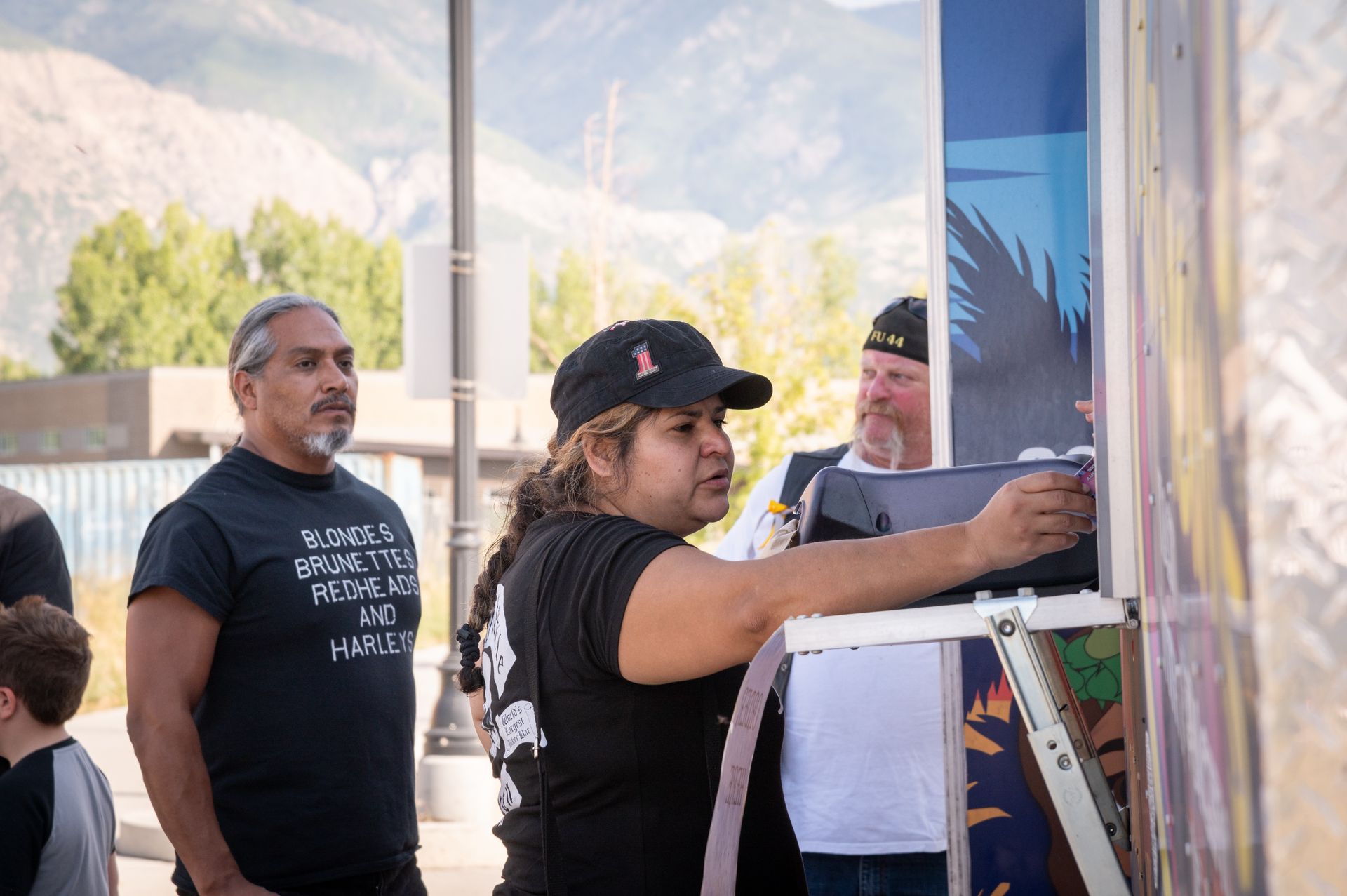 A woman is standing on a ladder painting a picture on a wall.