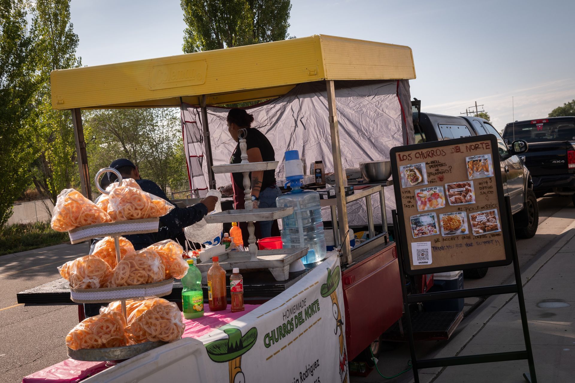 A man is working at a food stand in a parking lot.