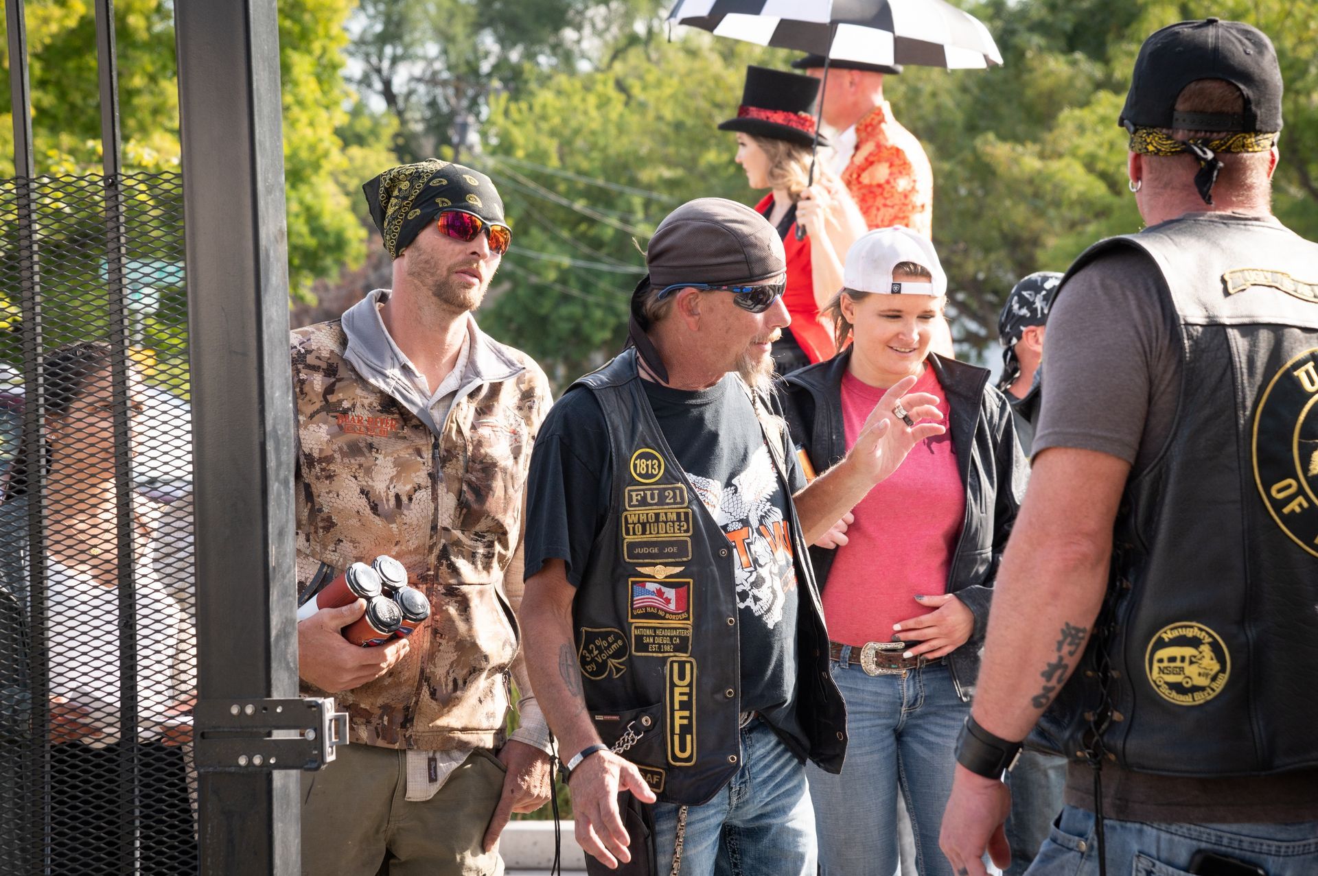 A group of people are standing in front of a fence talking to each other.