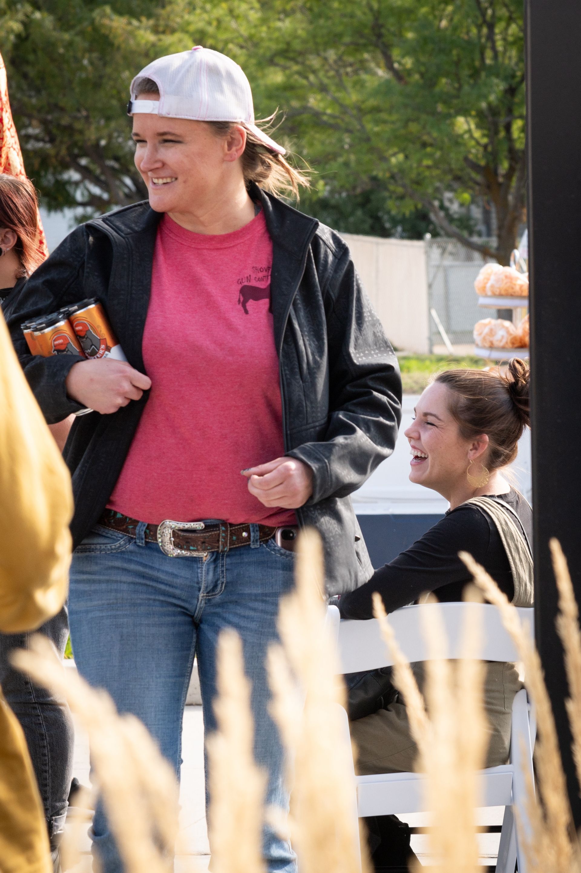 A woman wearing a baseball cap and a red shirt is standing next to a woman sitting on a bench.