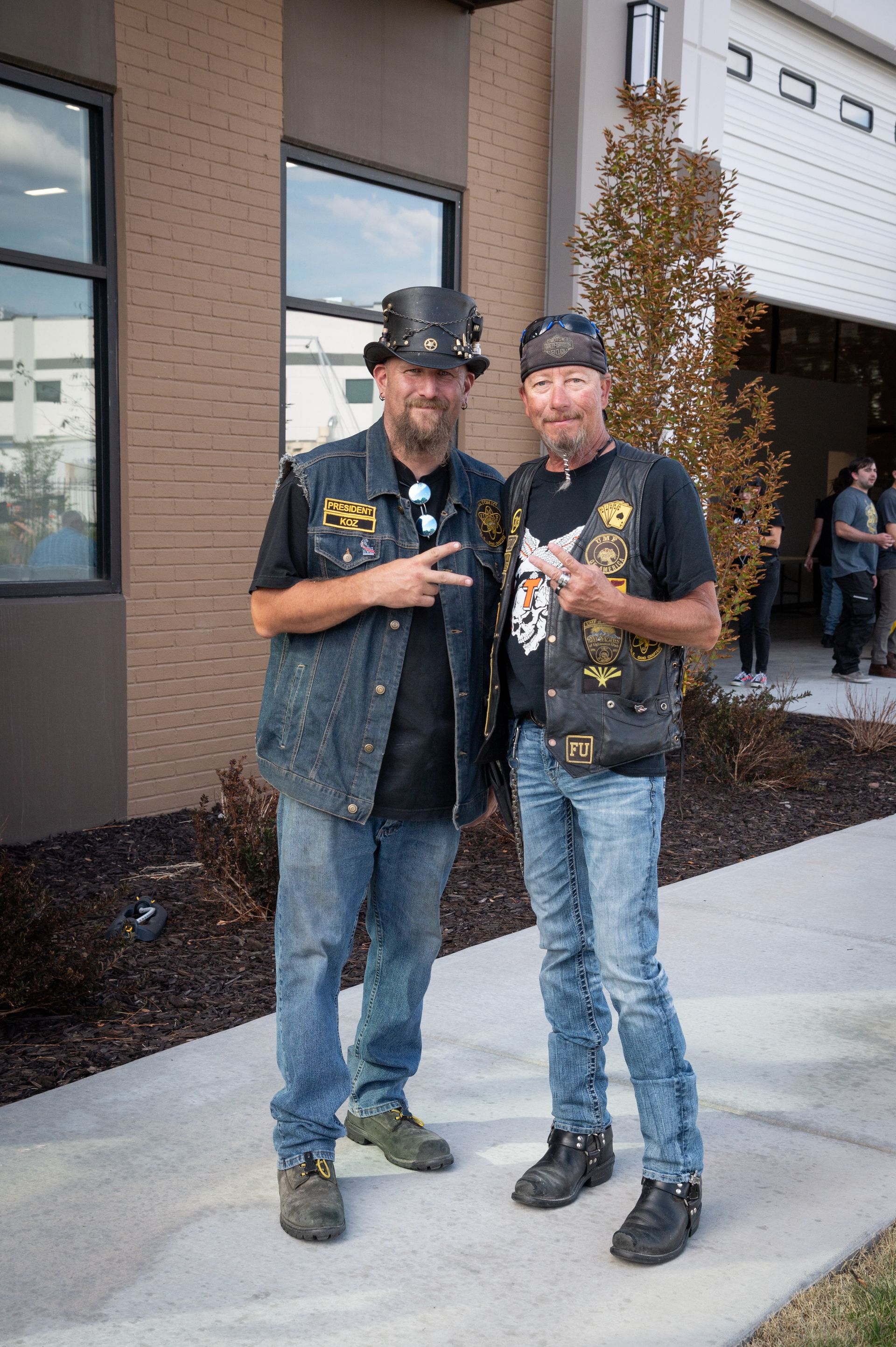 Two men are standing next to each other on a sidewalk in front of a building.
