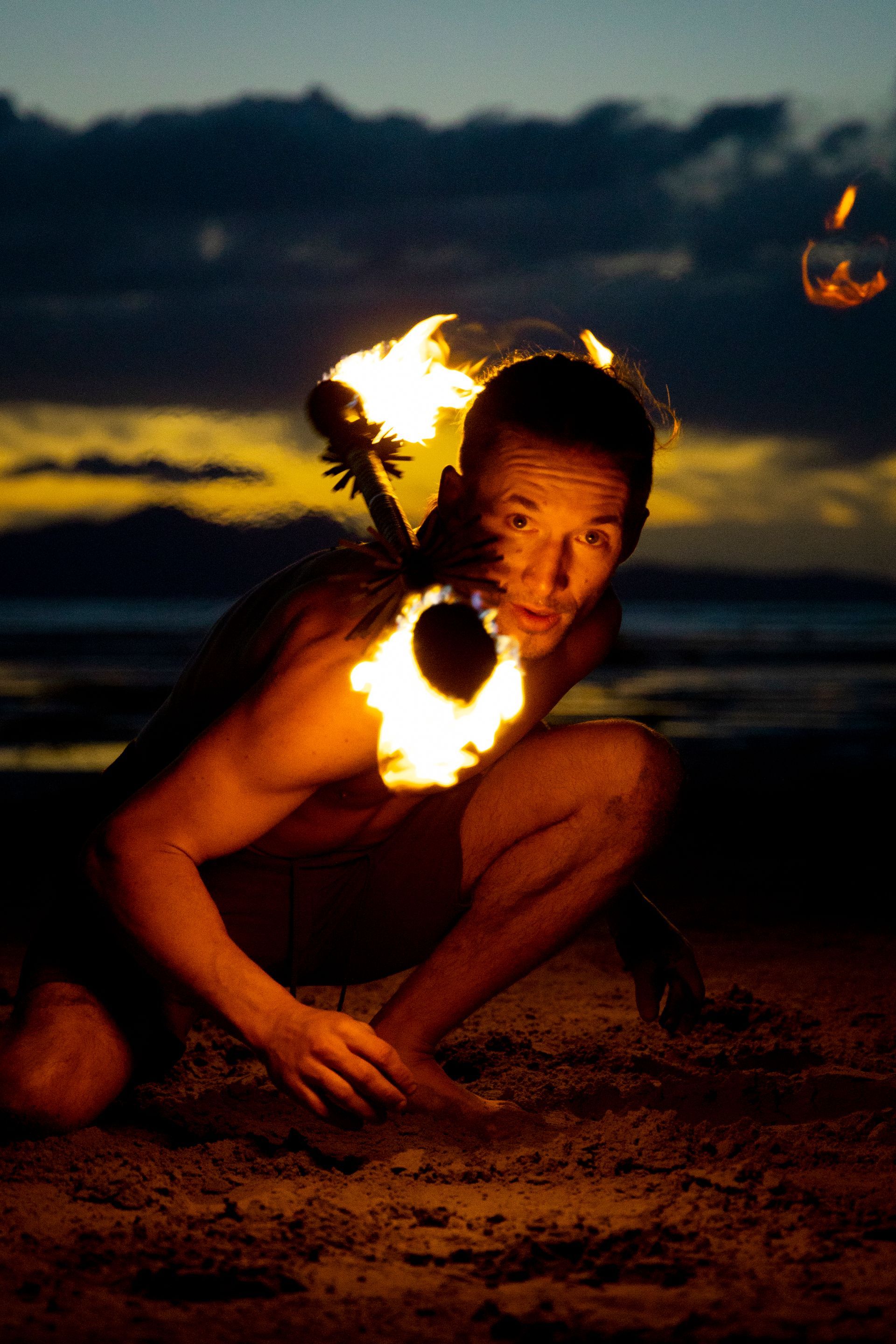 A man is kneeling on the beach holding a fire torch