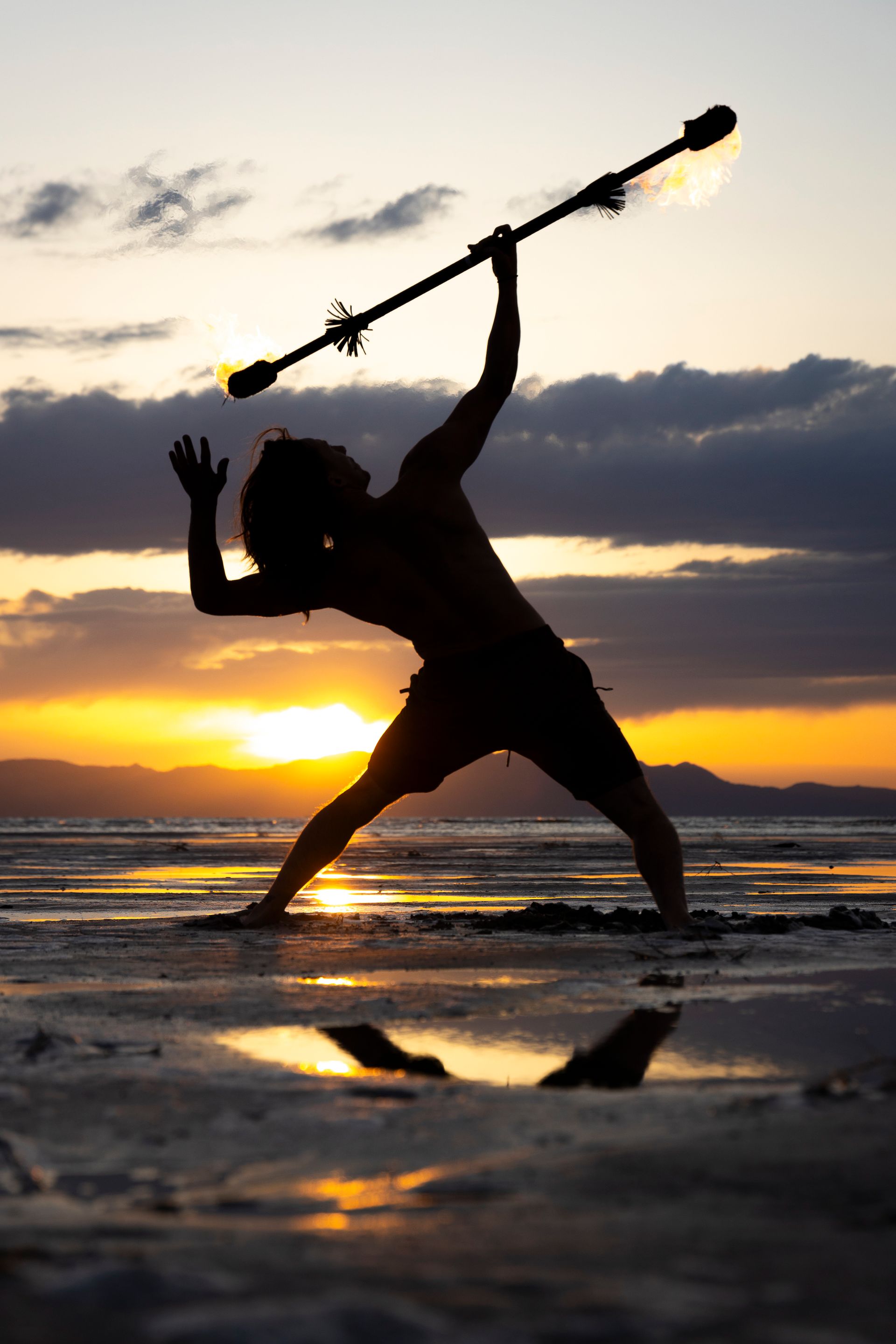 A silhouette of a person holding a stick on a beach at sunset.