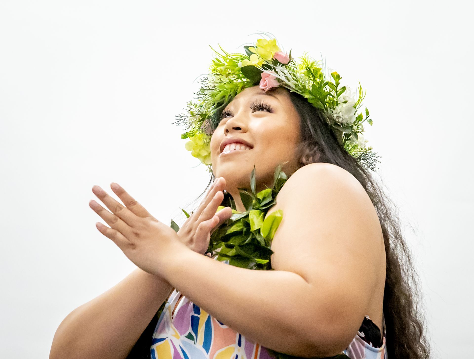 A woman wearing a lei and a flower crown is dancing.