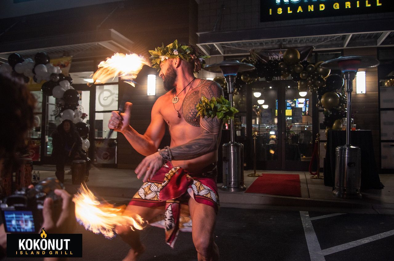 A shirtless man is holding a torch in front of a restaurant.