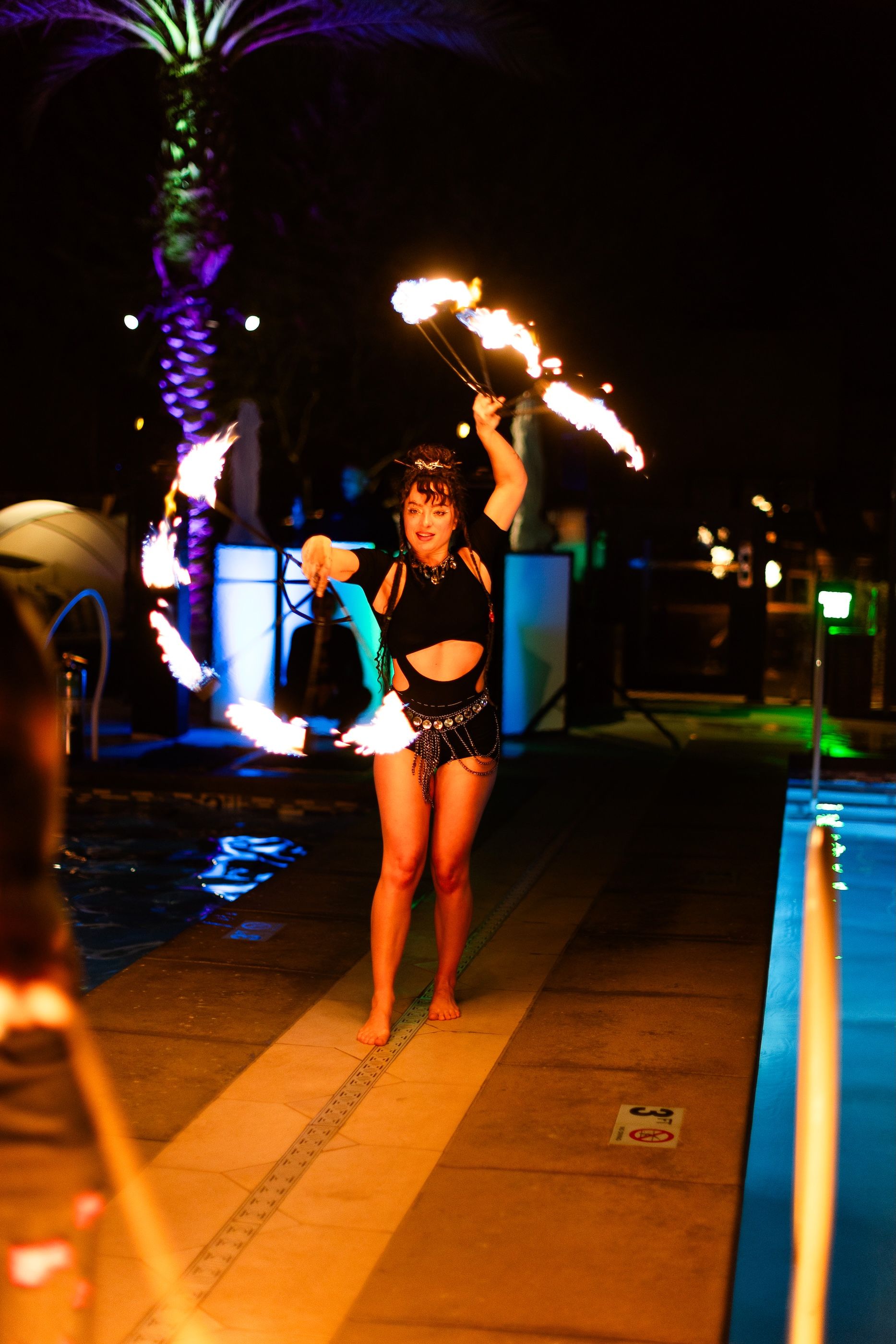 A woman is holding a pair of fire sticks in front of a pool.