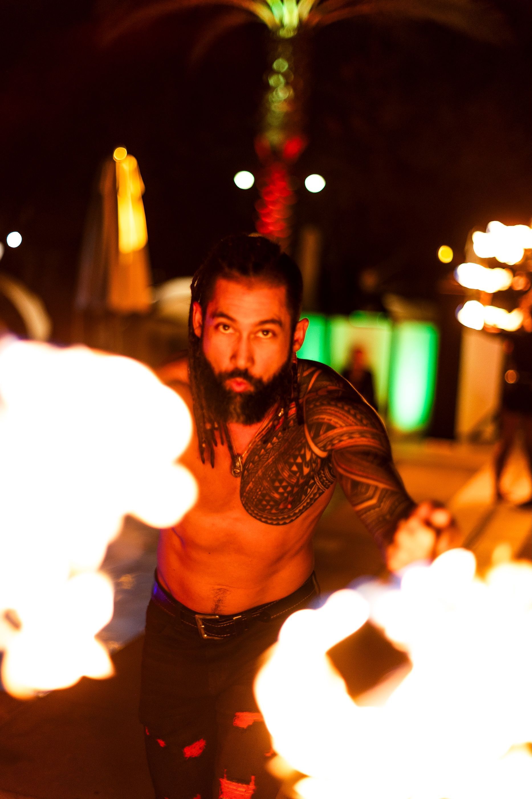 A shirtless man with a beard is holding a stick of fire