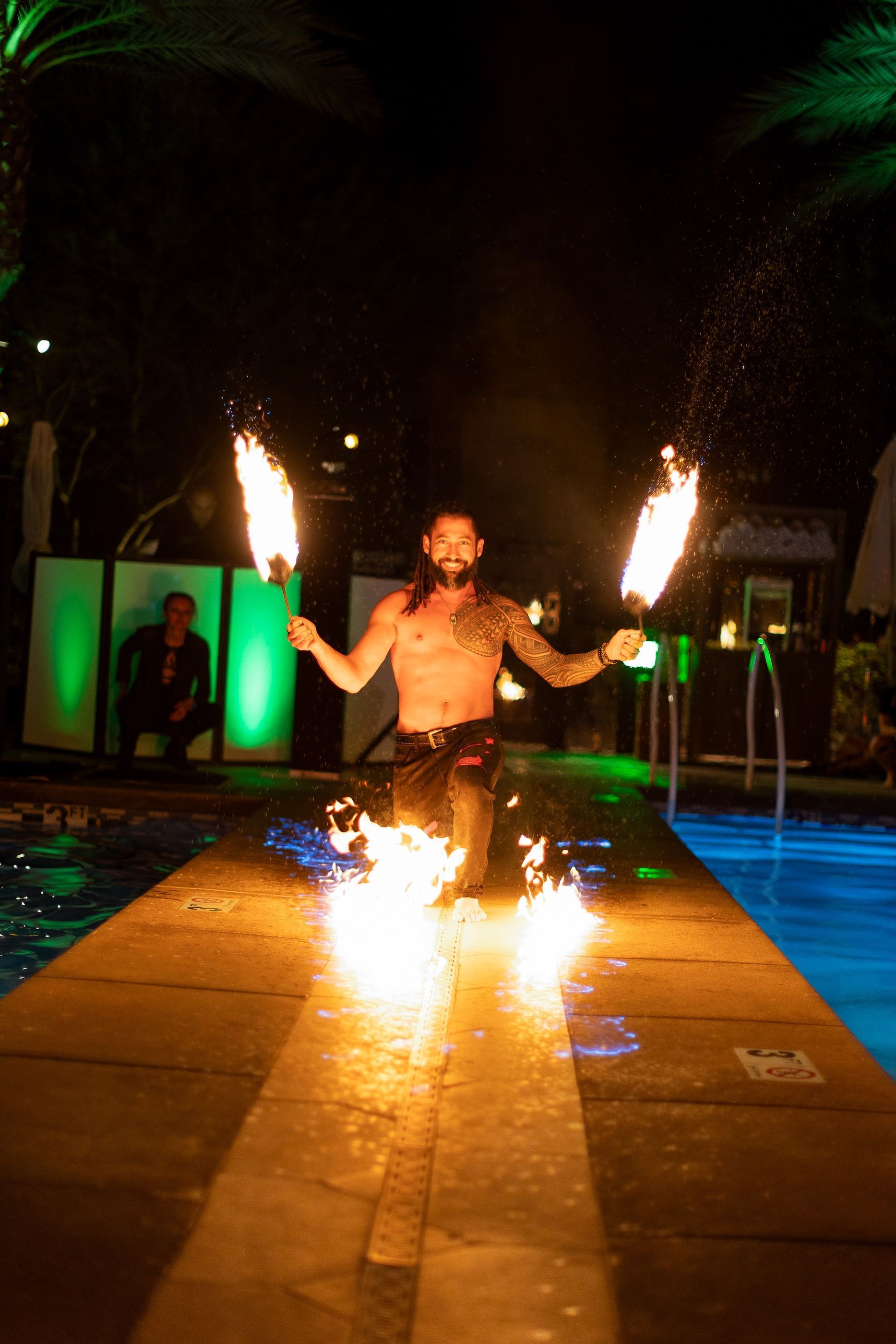 A man is holding two fire torches in front of a swimming pool.
