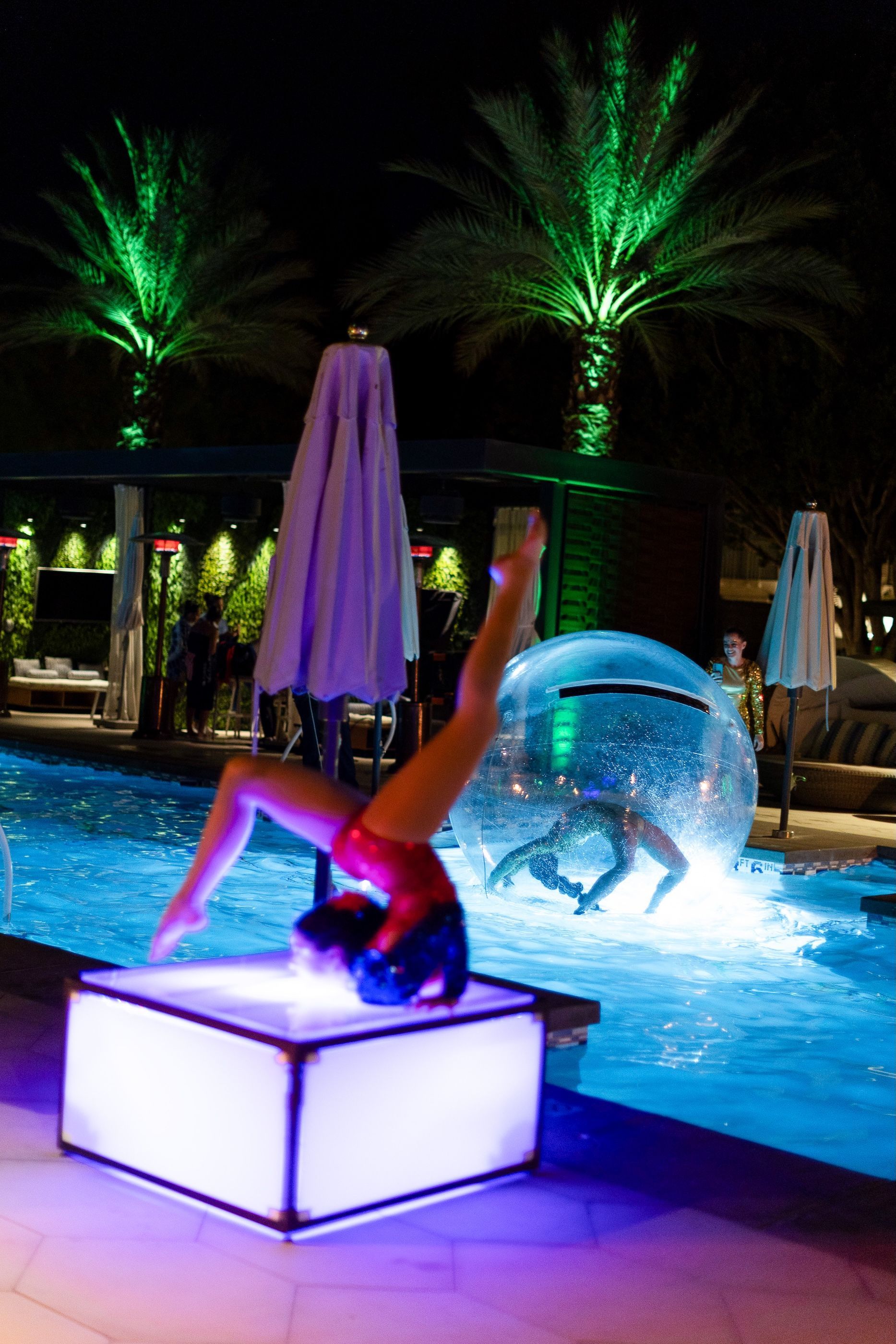 A woman is doing a handstand in front of a swimming pool at night.
