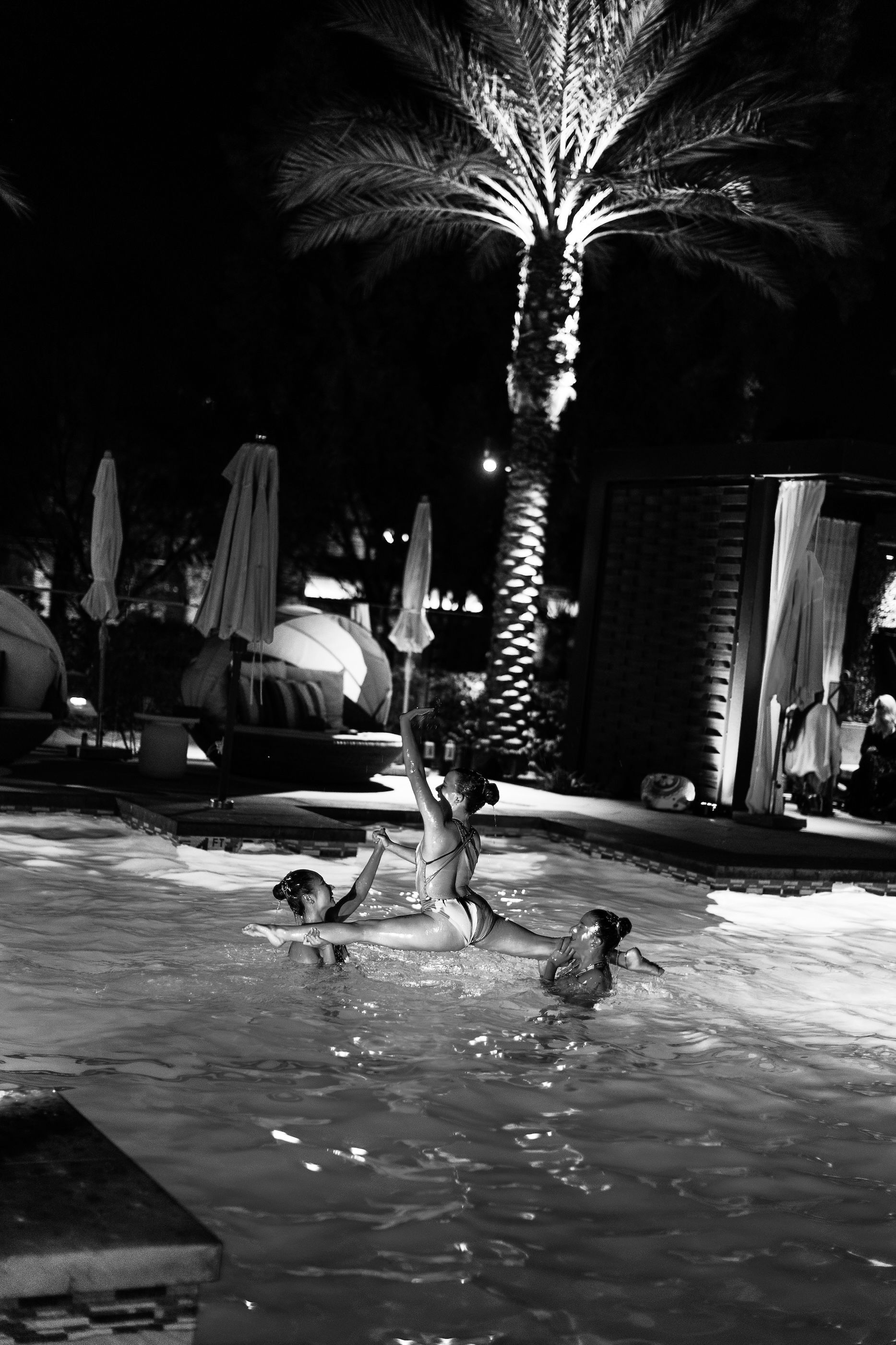 A group of people are swimming in a pool at night.