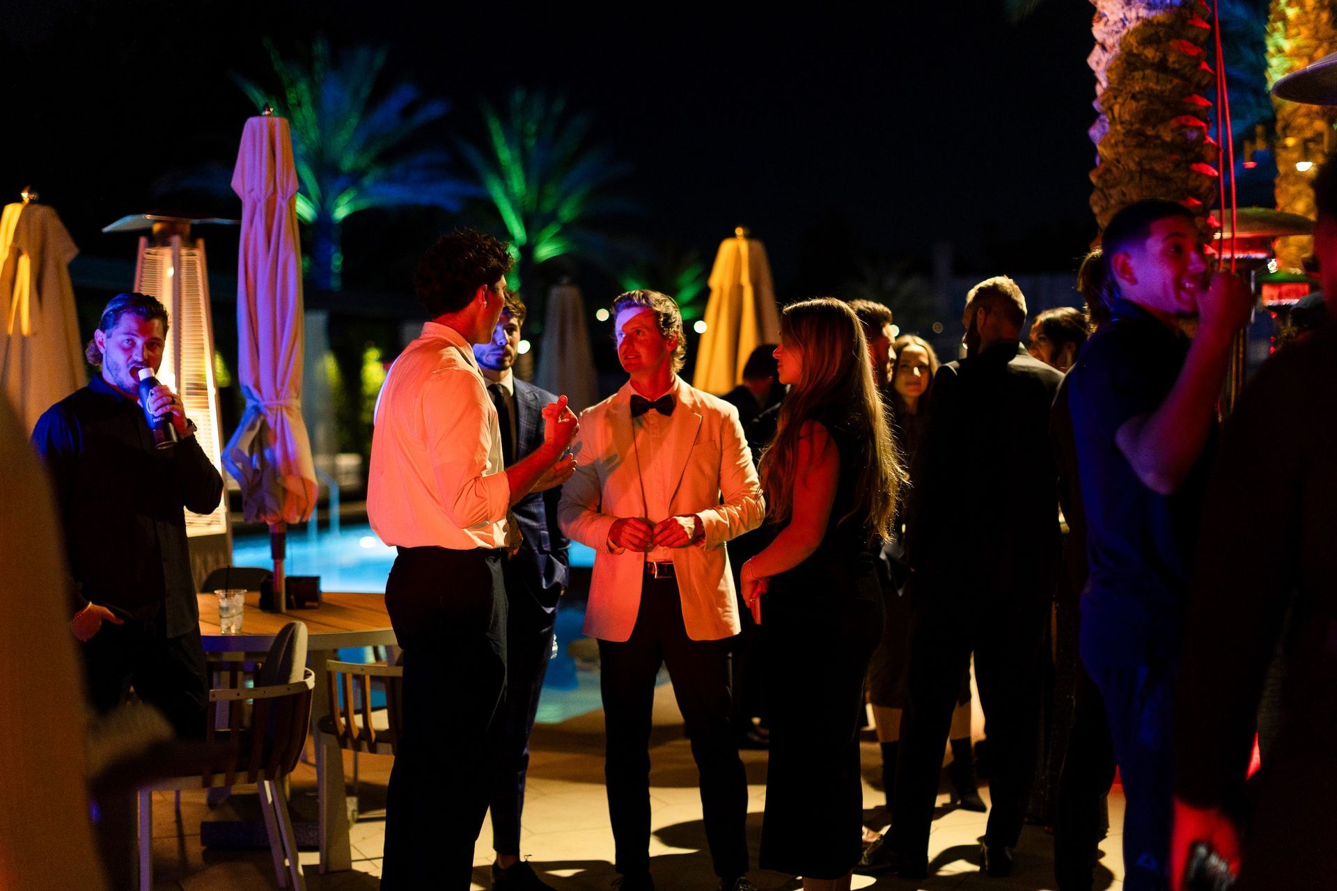 A group of people are standing around a pool at night.