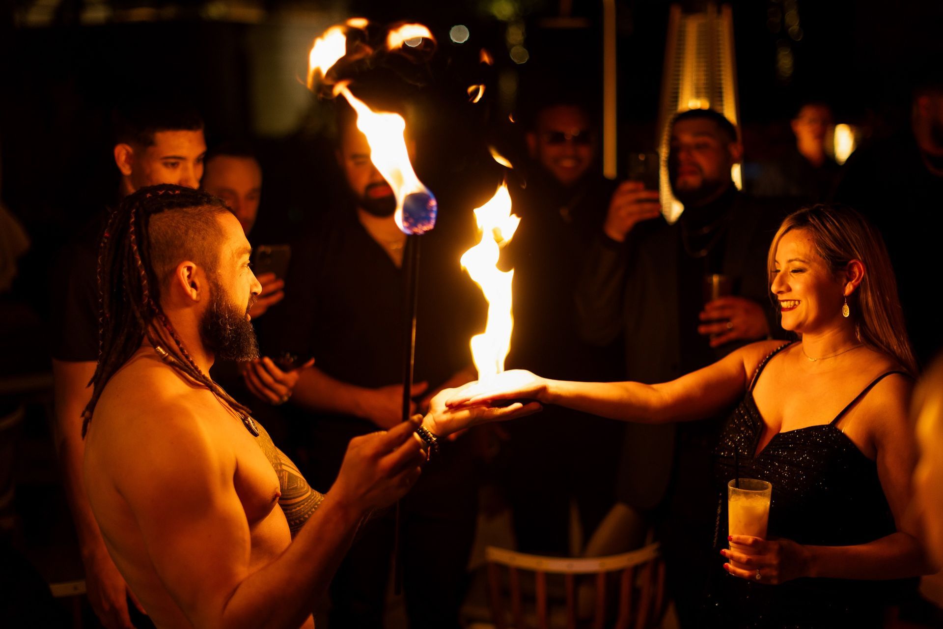 A man is holding a fireball in his hand while a woman holds a drink.