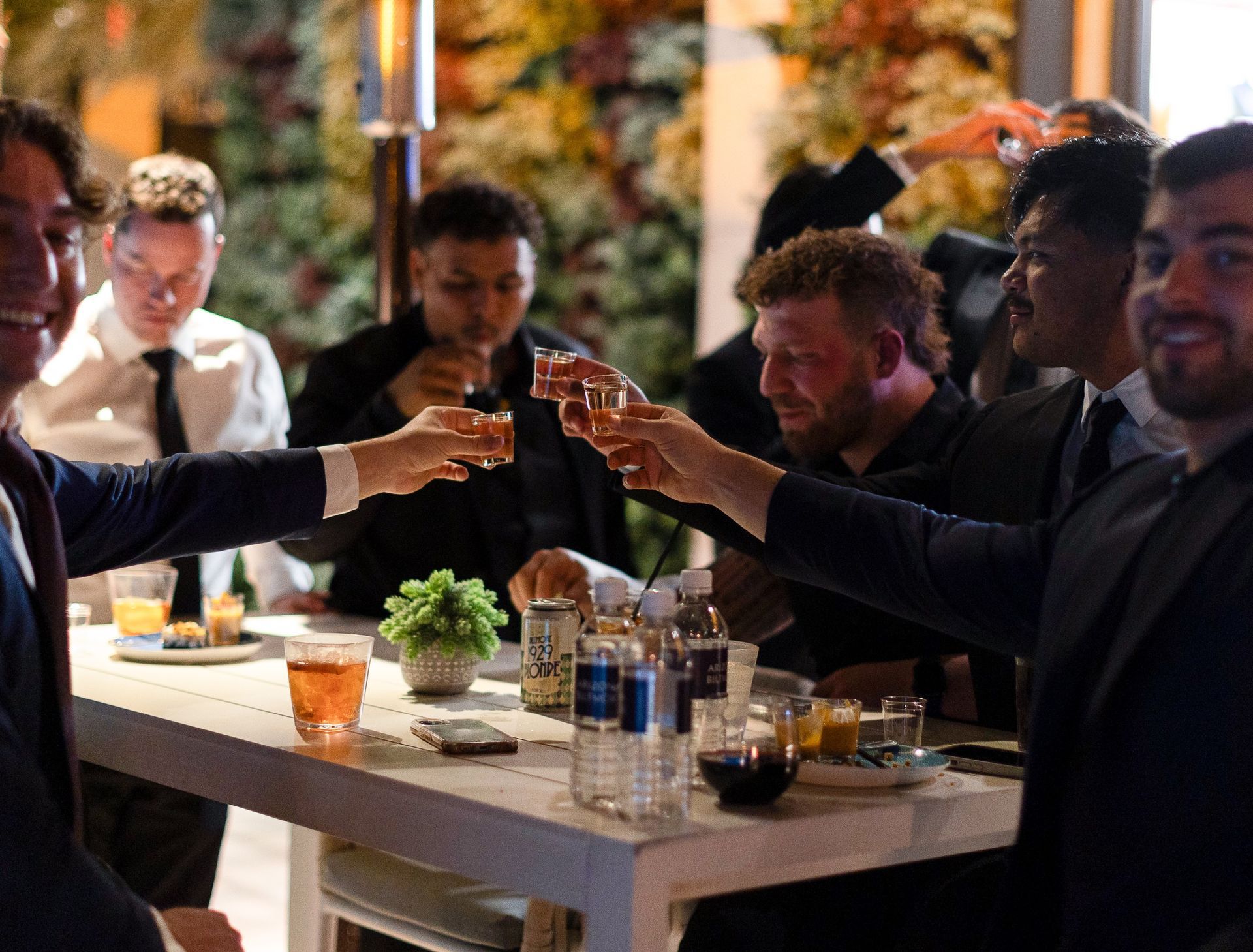 A group of men are sitting at a table toasting with shot glasses.