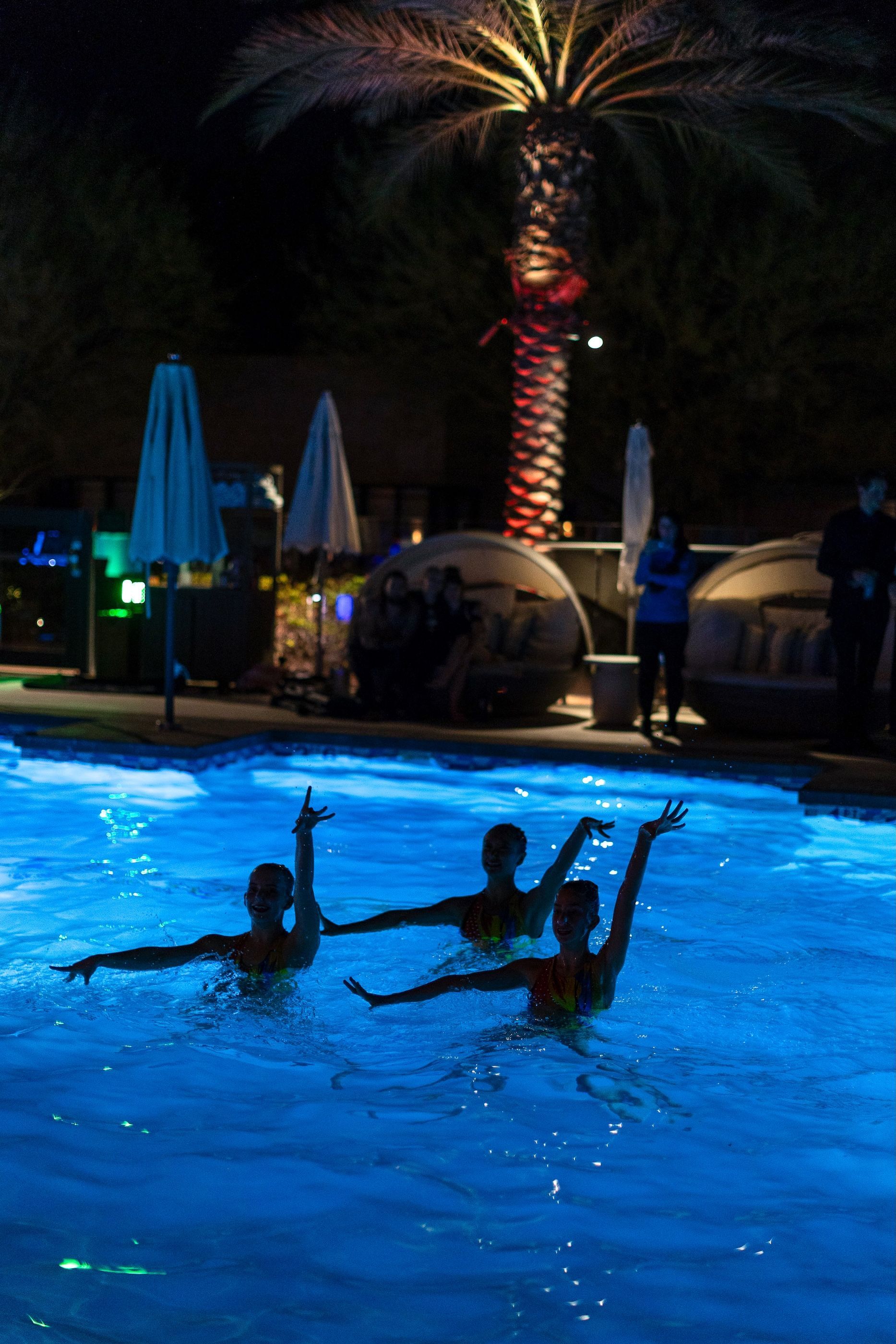 A group of people are swimming in a pool at night