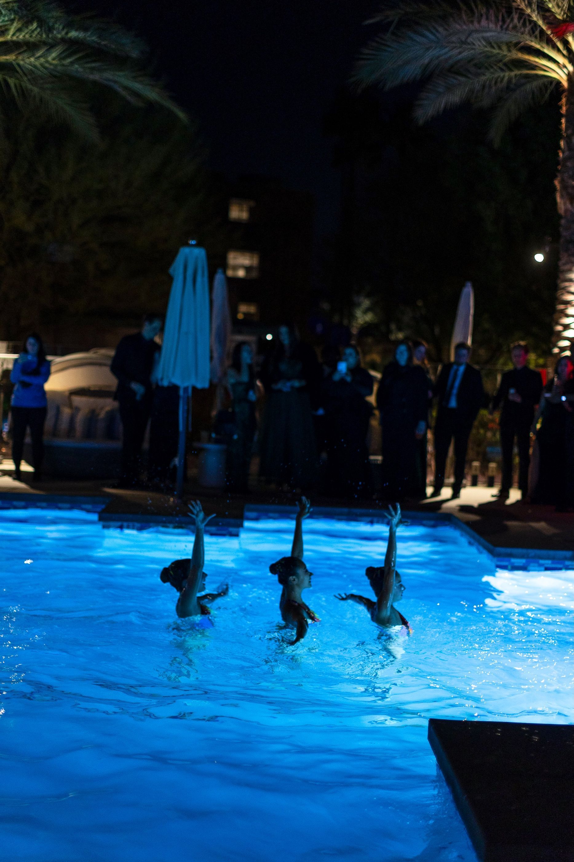 A group of people are swimming in a pool at night